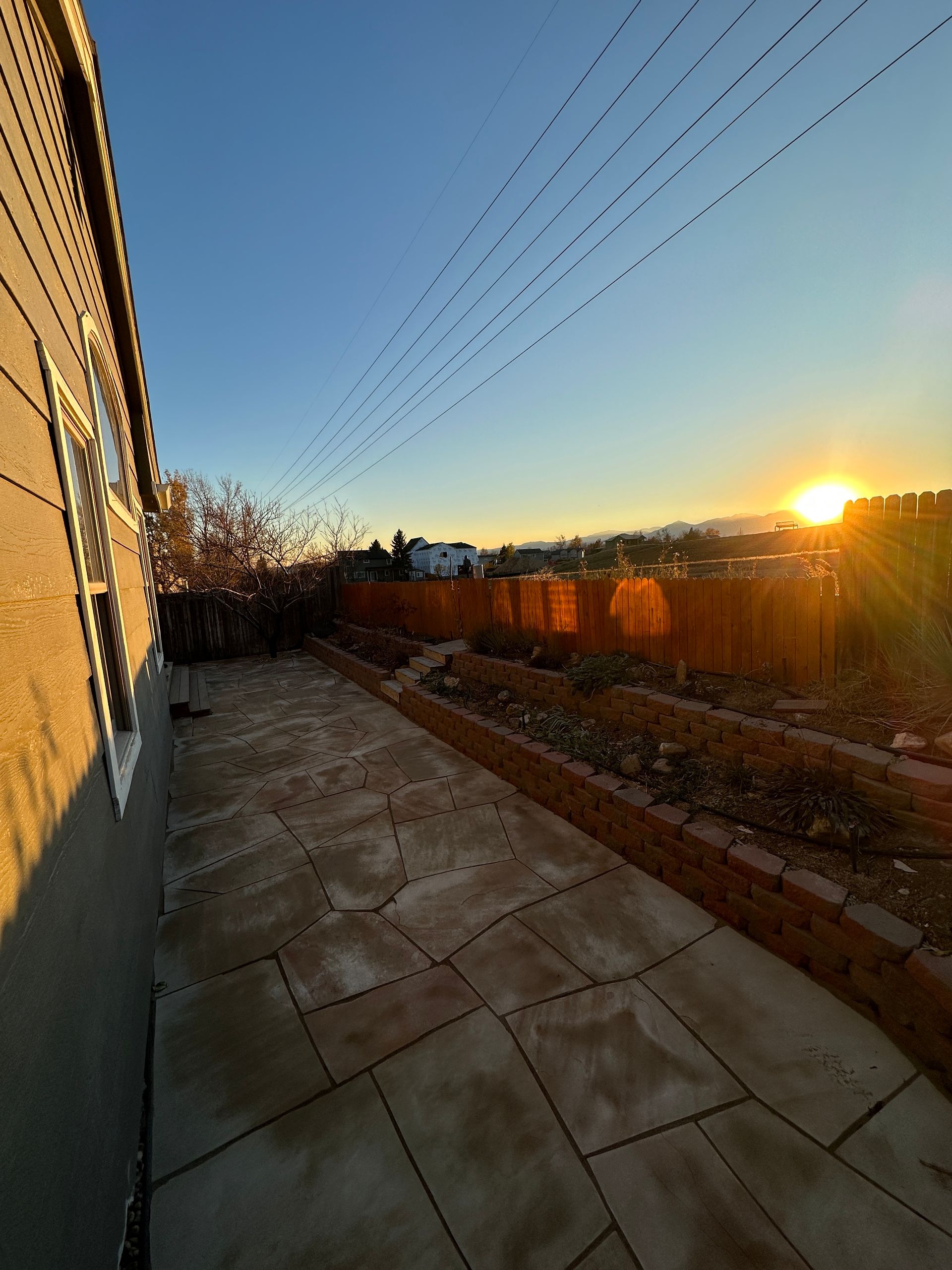 Backyard patio with setting sun, brown stone tiles, and a wooden fence.
