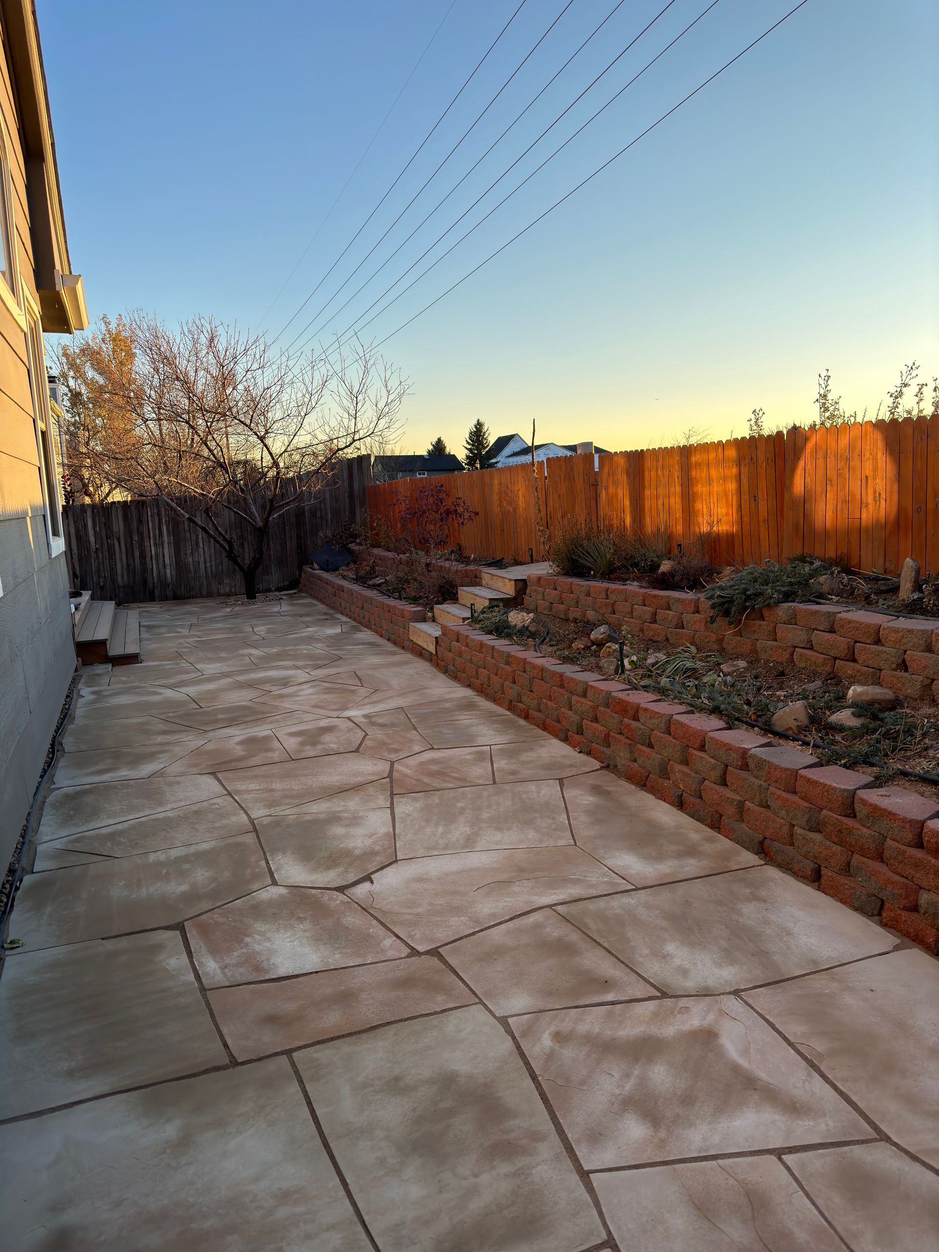 Backyard with brick planters, flagstone patio, and wooden fence at dusk.
