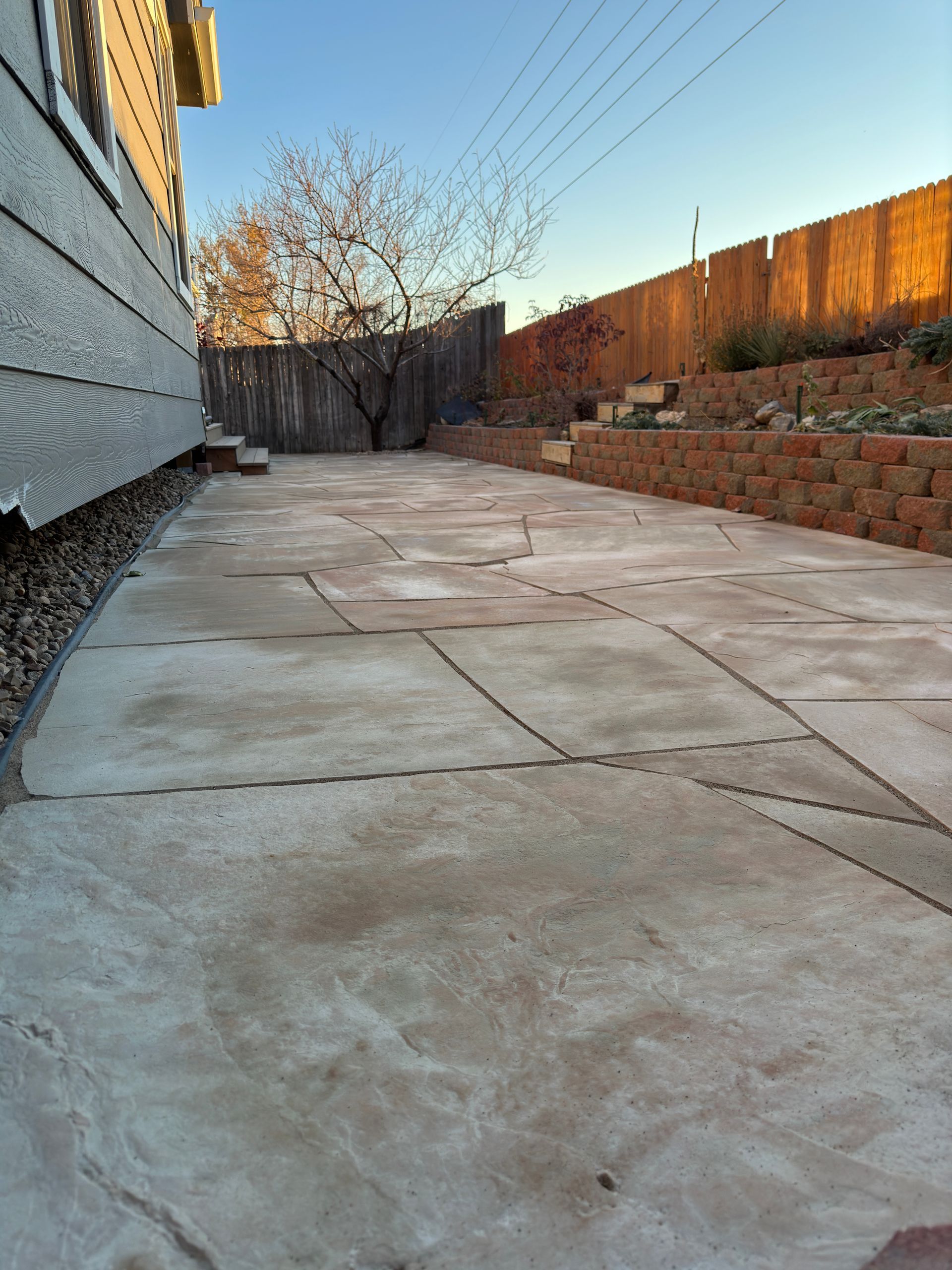Concrete patio with weathered stone pattern, next to a house and a wooden fence.