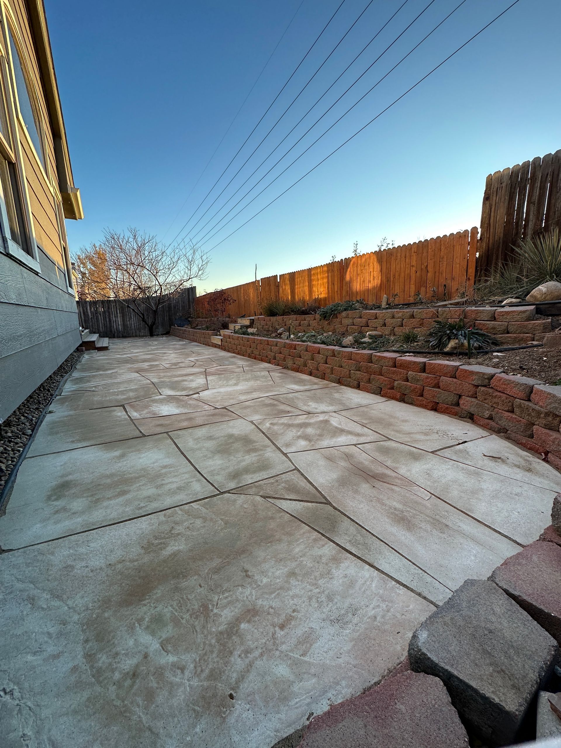 Concrete patio with brick retaining wall and wooden fence against a blue sky.