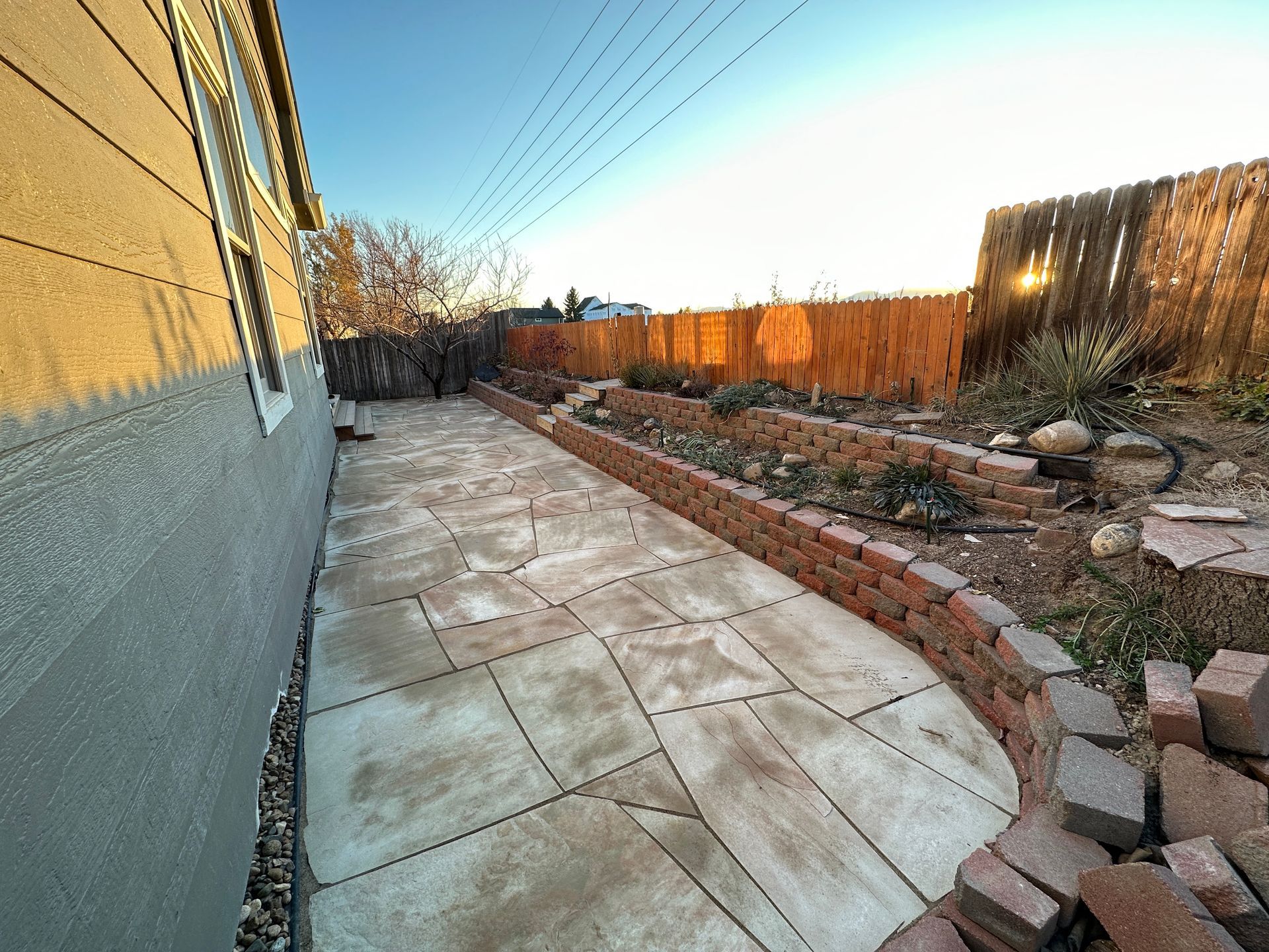 Backyard with stone path, brick planters, and wooden fence bathed in sunlight.