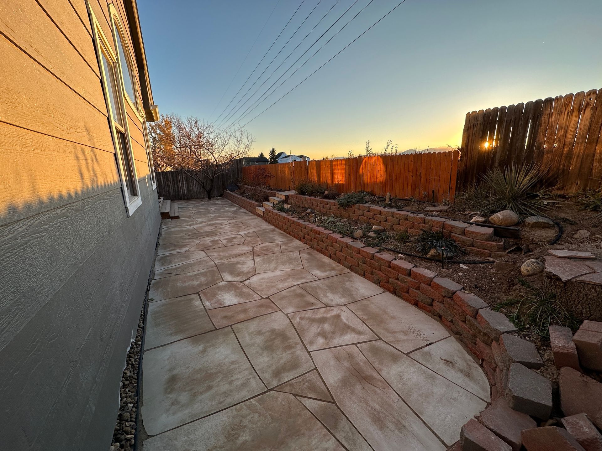 Patio with stone pavers and brick retaining wall, against a fence at sunset.