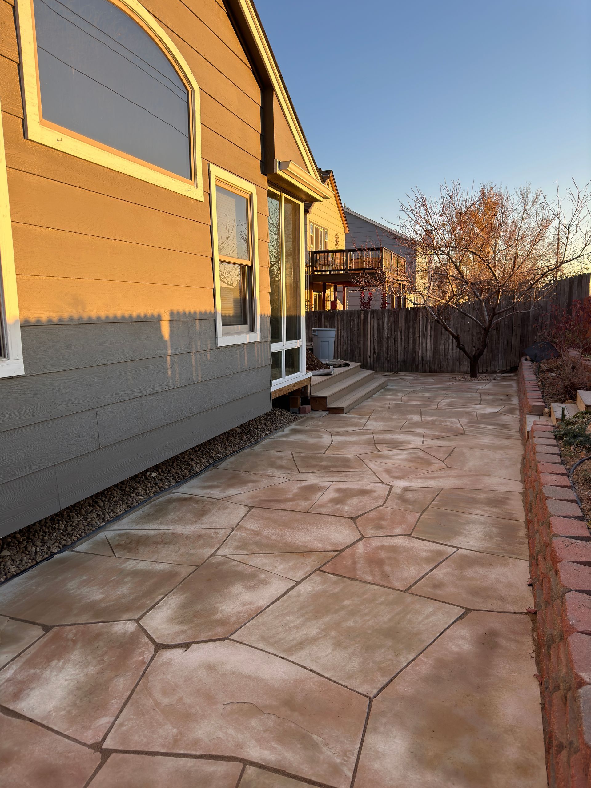 Backyard patio with flagstone, siding on a house, and a wooden fence.
