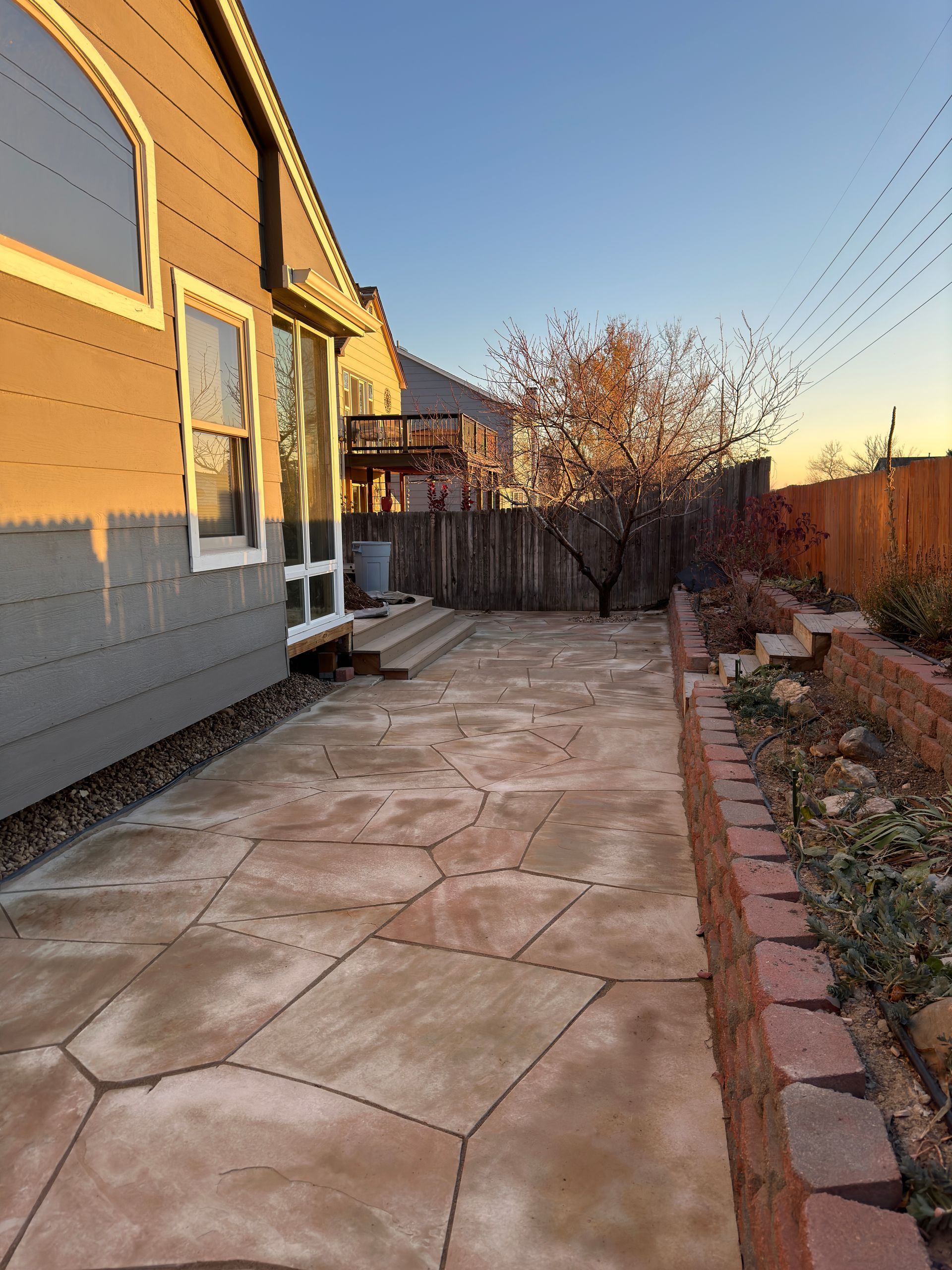 A backyard patio with stamped concrete, a brick border, and a wooden fence, under a blue sky.