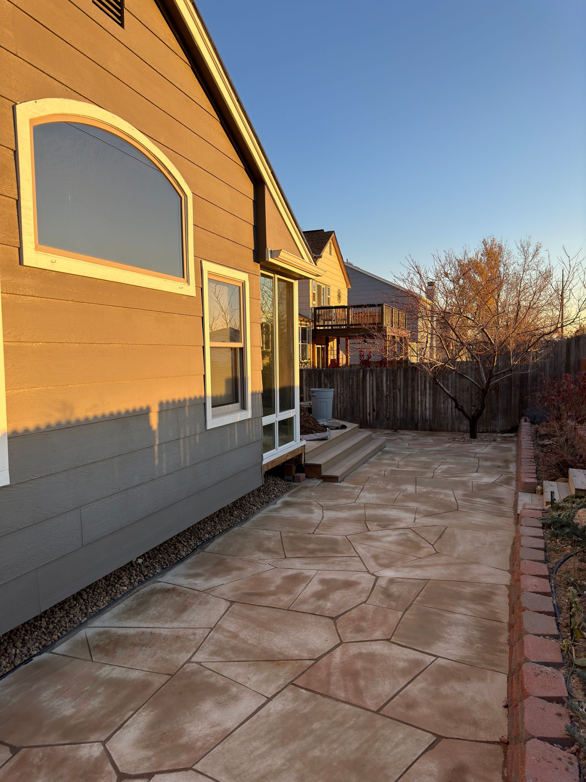 Back patio with stone pavers, house, wooden fence, and neighboring house with a deck.