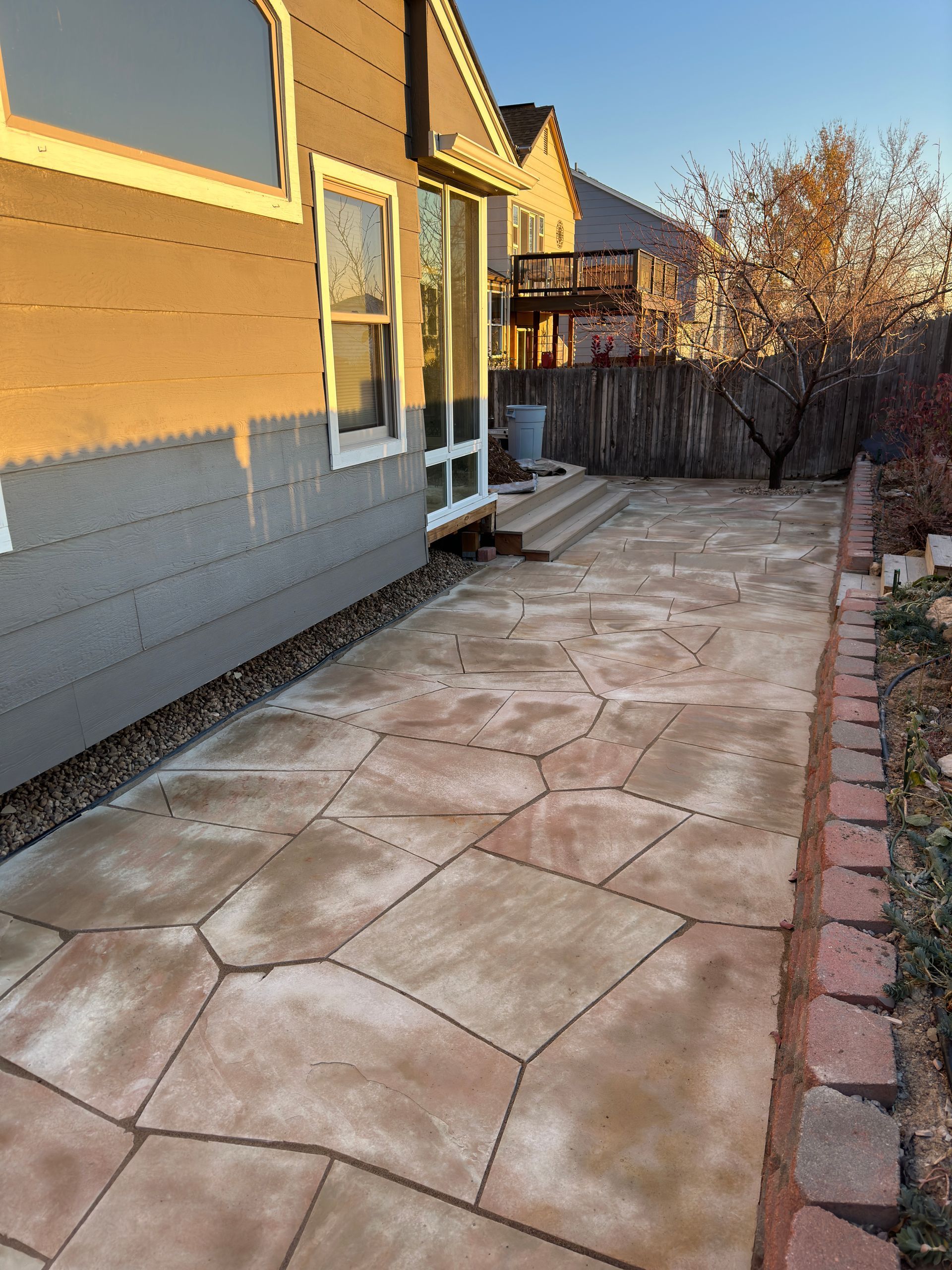 Stone patio next to a house with steps and a brick border.