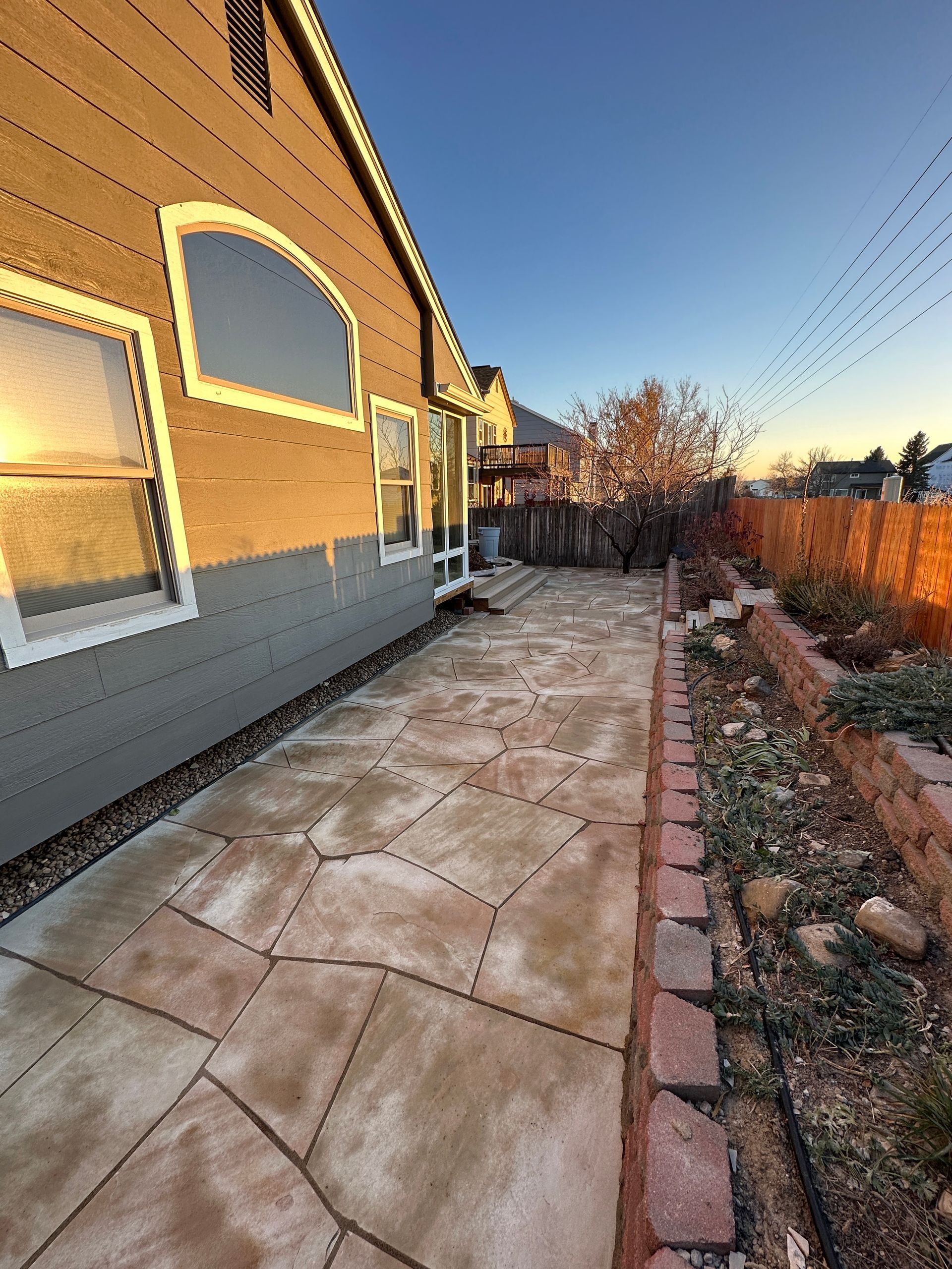 Backyard patio with stone paving, house siding, and a low brick border.