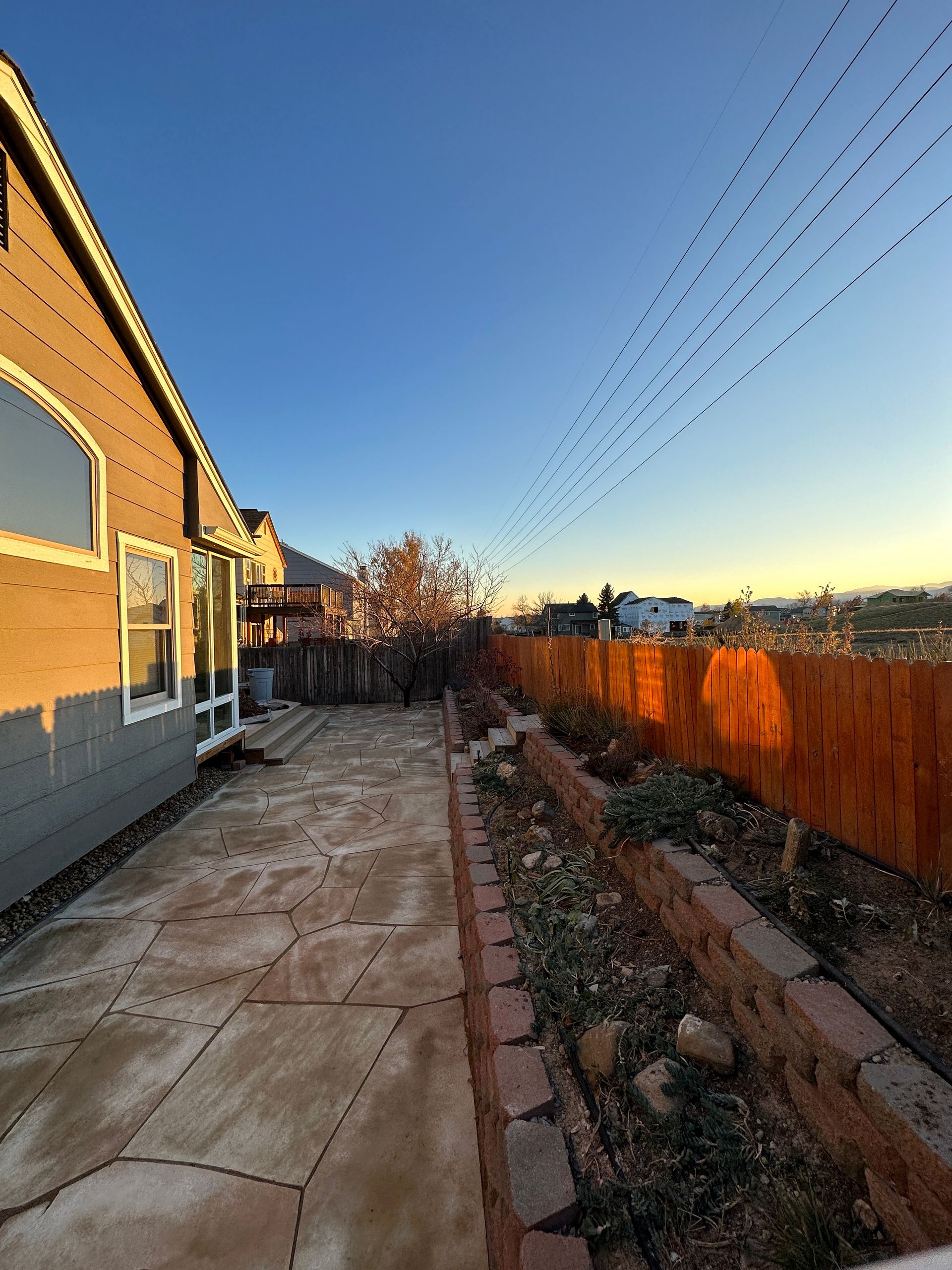 Backyard patio with wooden fence and garden beds under a blue sky at sunset.