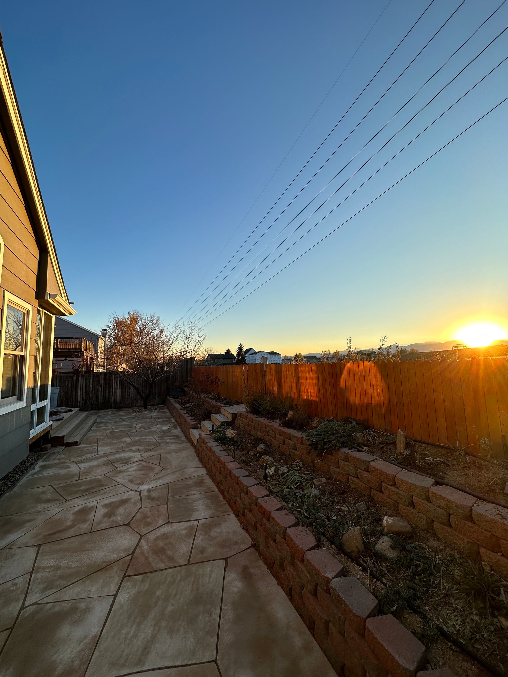 Backyard view at sunset with a patio, garden beds, and clear blue sky.