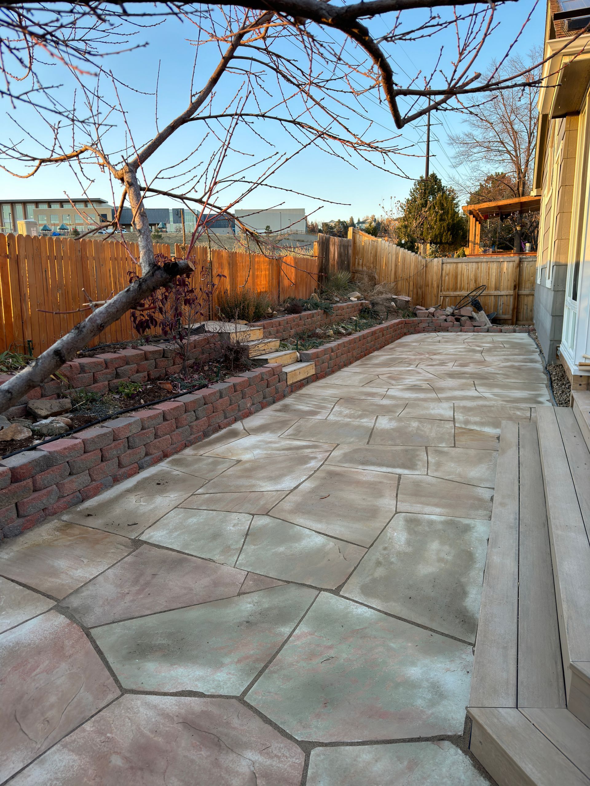 Backyard patio with flagstone, raised brick planters, and a wooden fence.
