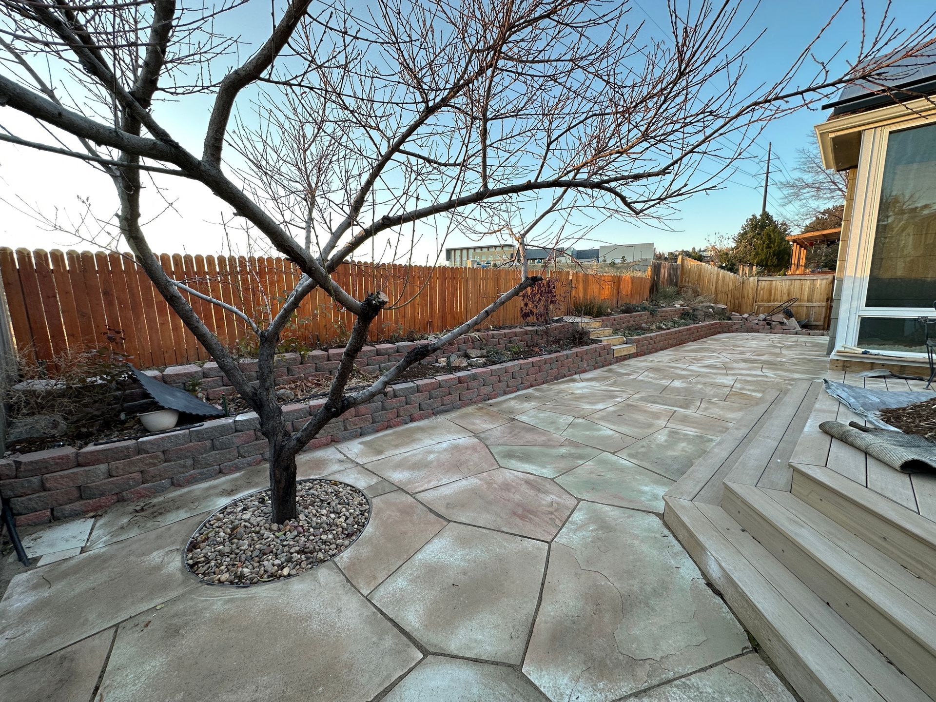 Backyard with flagstone patio, brick retaining walls, bare tree, and wooden fence.