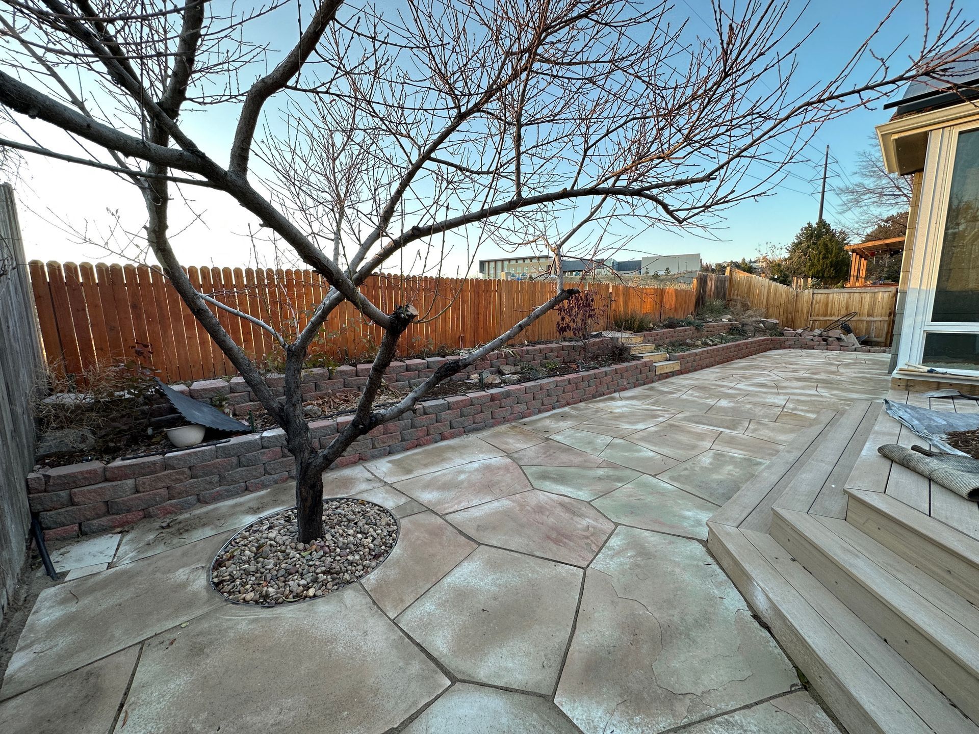 Backyard with stone patio, tree, raised beds, wooden fence.