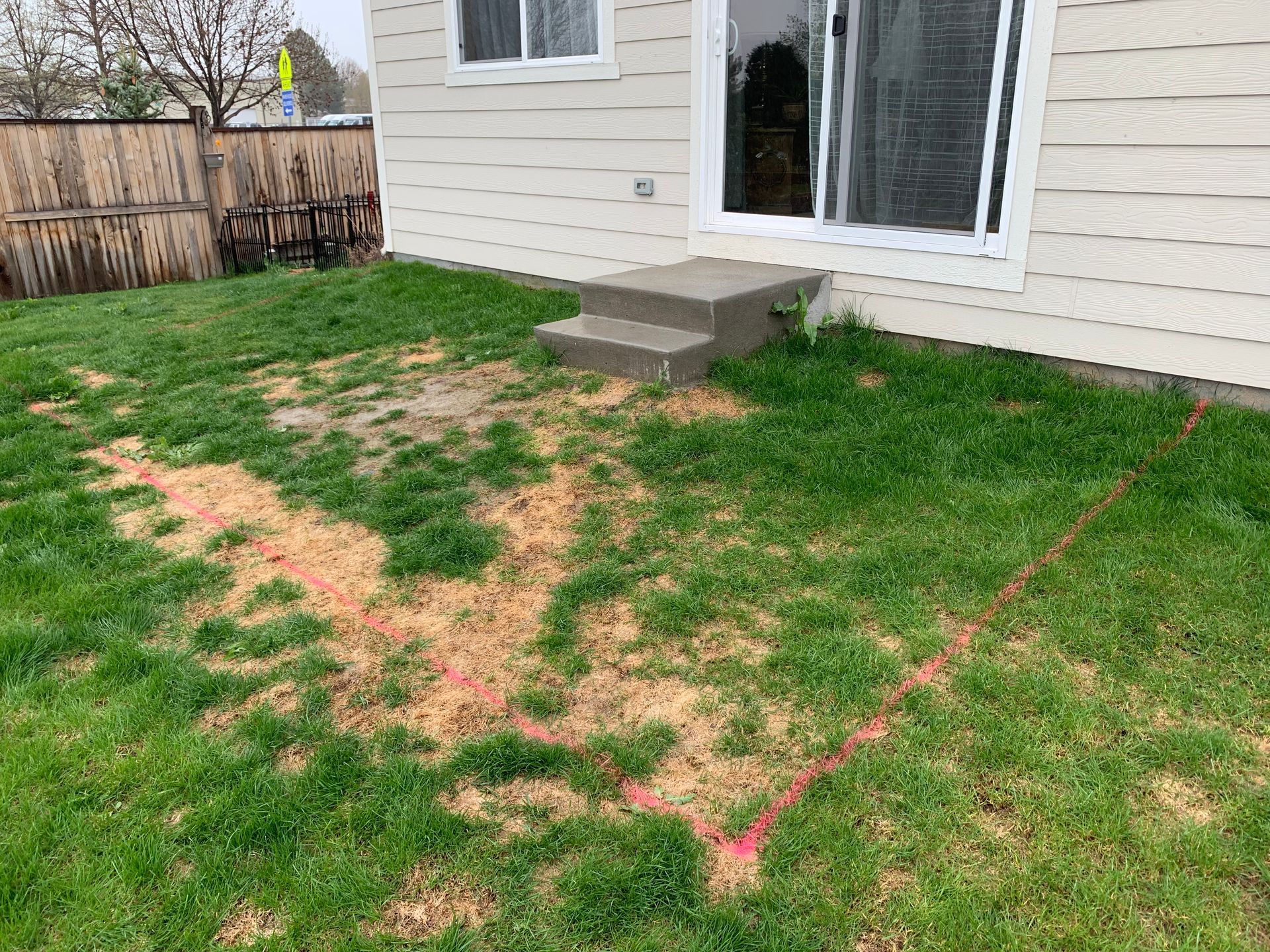 Grassy backyard with a concrete step, marked construction area, and house with a sliding glass door.