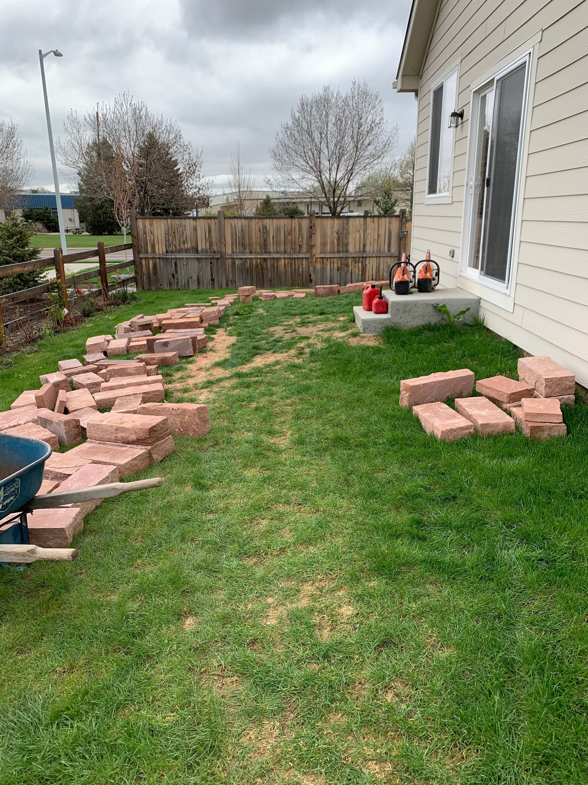 Backyard with bricks laid out on grass, next to a house and fence.