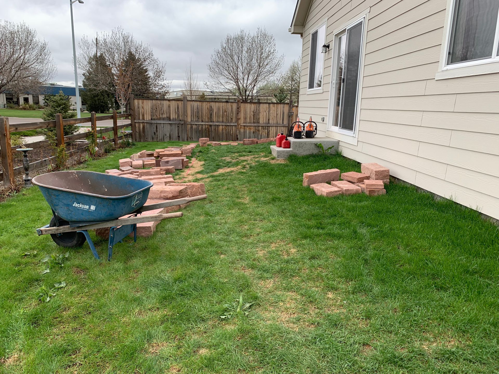 Lawn with wheelbarrow, bricks, and house; a pathway is being built.