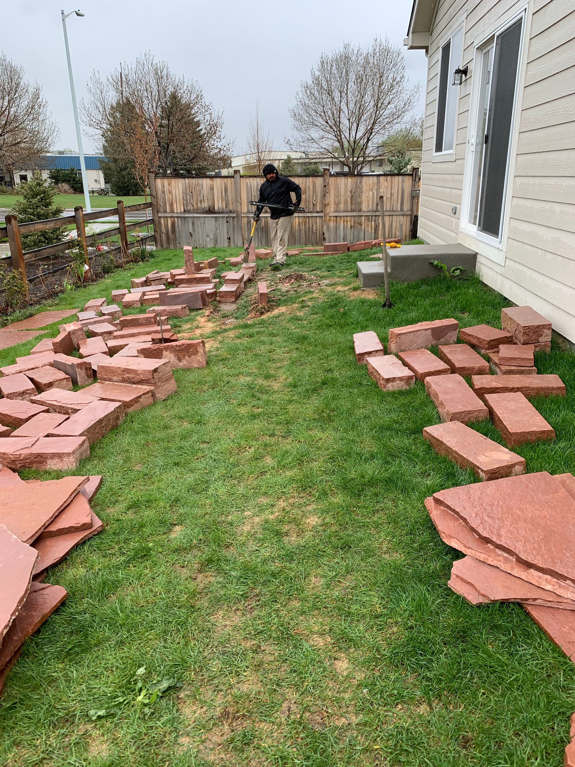 Person laying red brick pavers on grass next to a house.