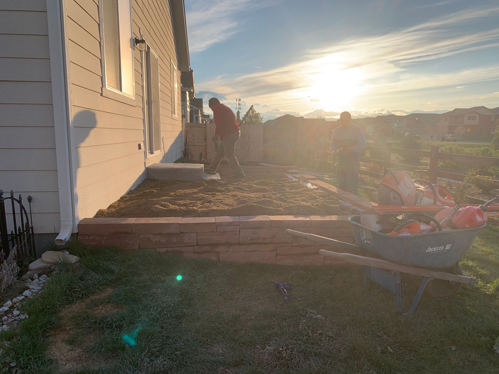 People building a retaining wall next to a house with a sunset in the background.