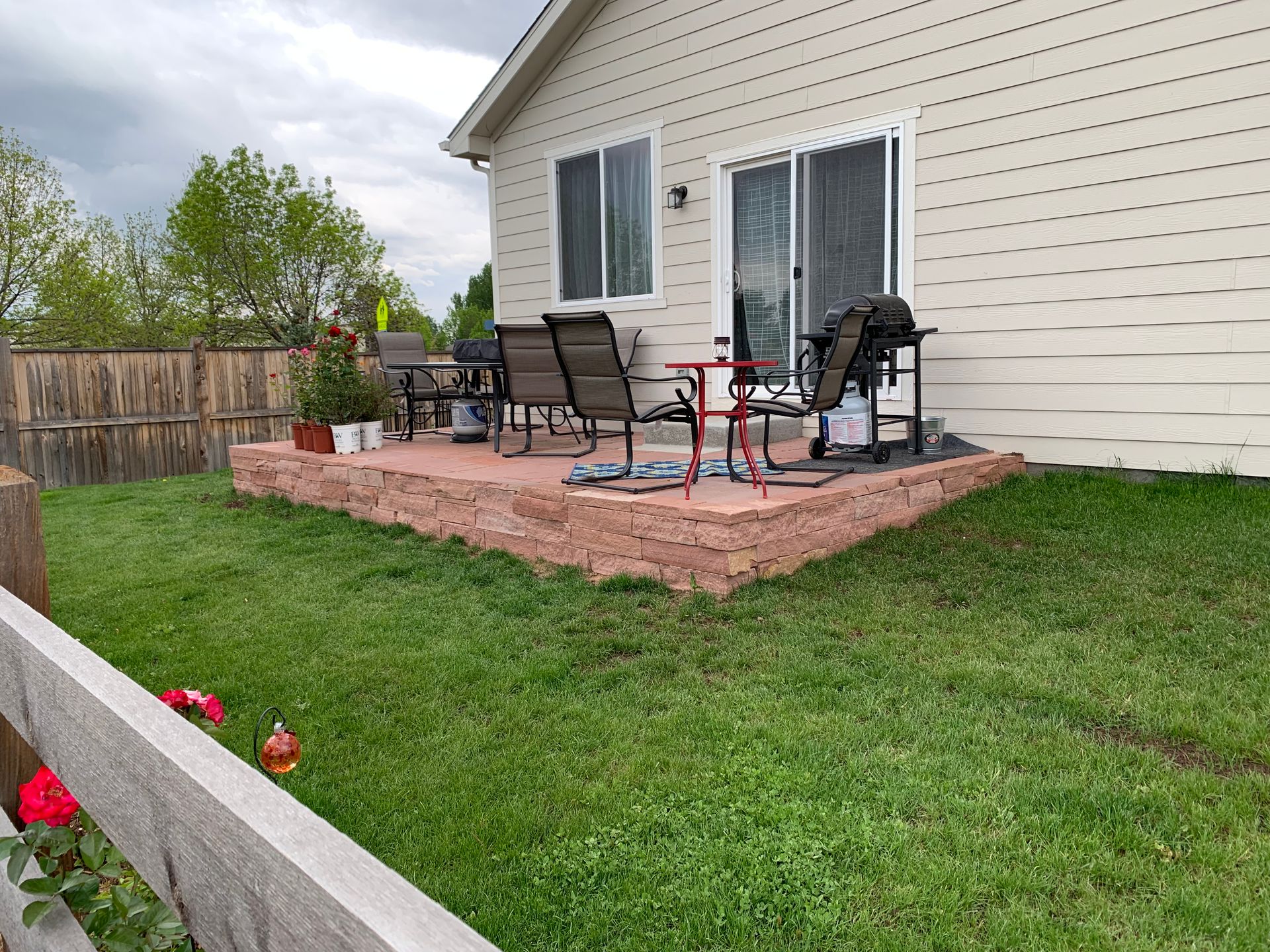 Patio with red brick border, grass lawn, outdoor furniture, and sliding glass door.
