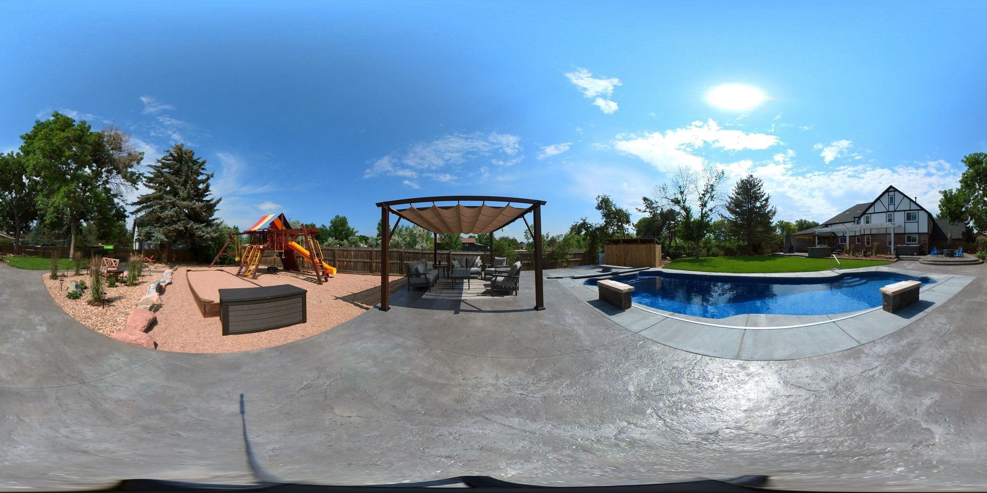 Backyard with pool, playground, pergola, and lush green lawn under a bright blue sky.