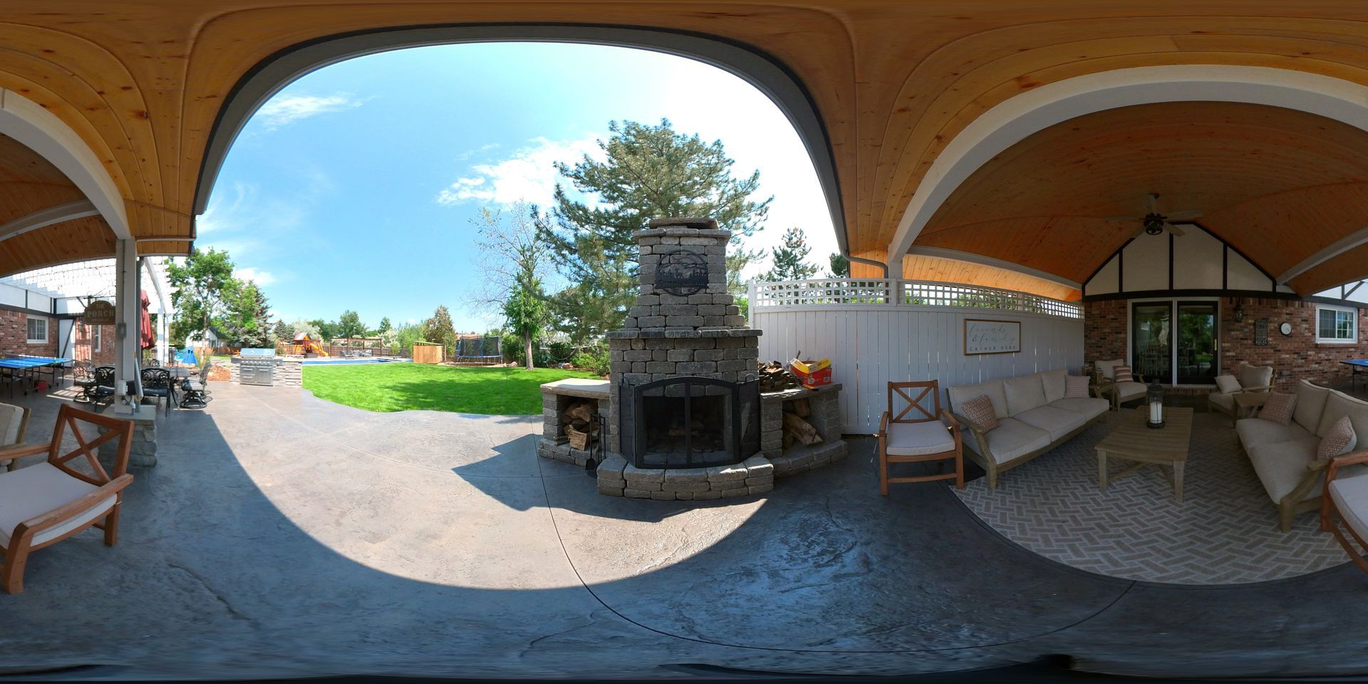 Outdoor patio with fireplace, seating, and view of a yard on a sunny day.