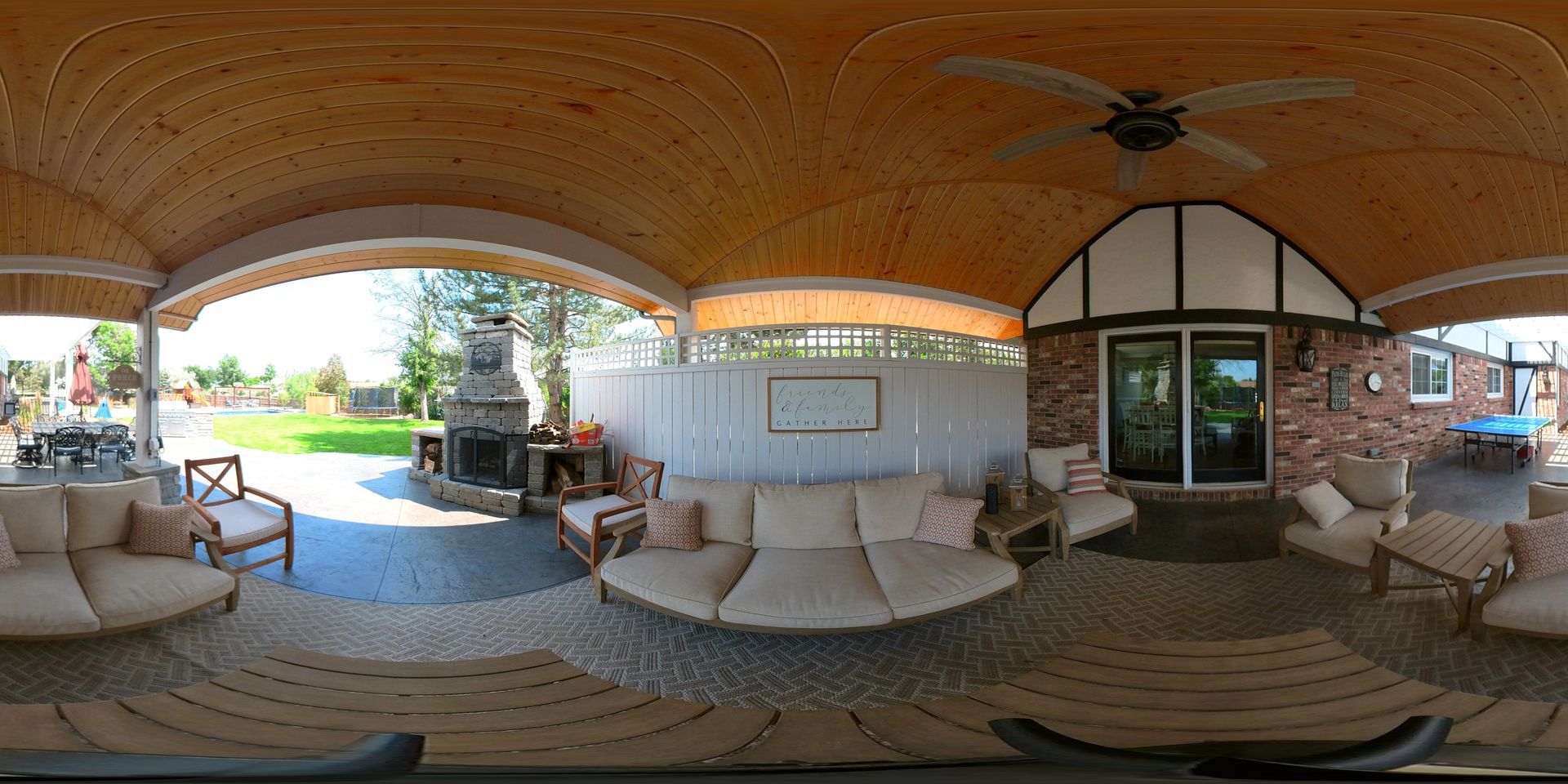A covered outdoor patio with seating, a fireplace, and a ceiling fan.