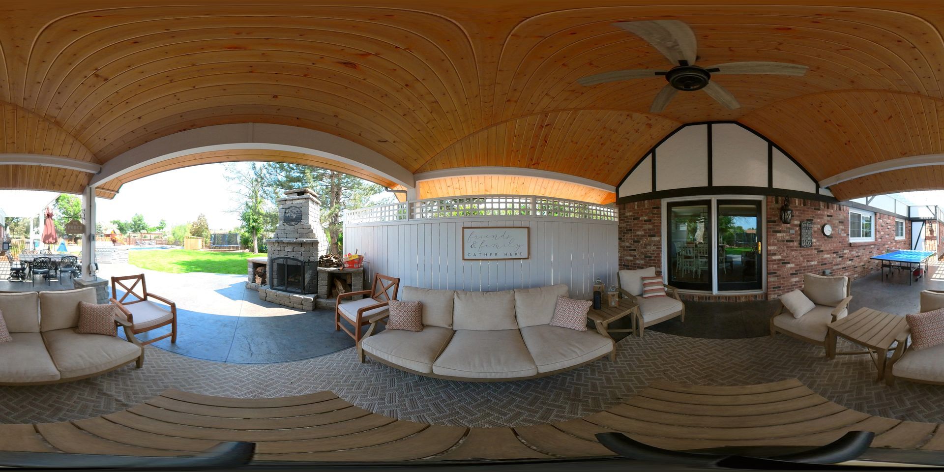 An outdoor patio with a seating area, fireplace, and arched wooden ceiling.