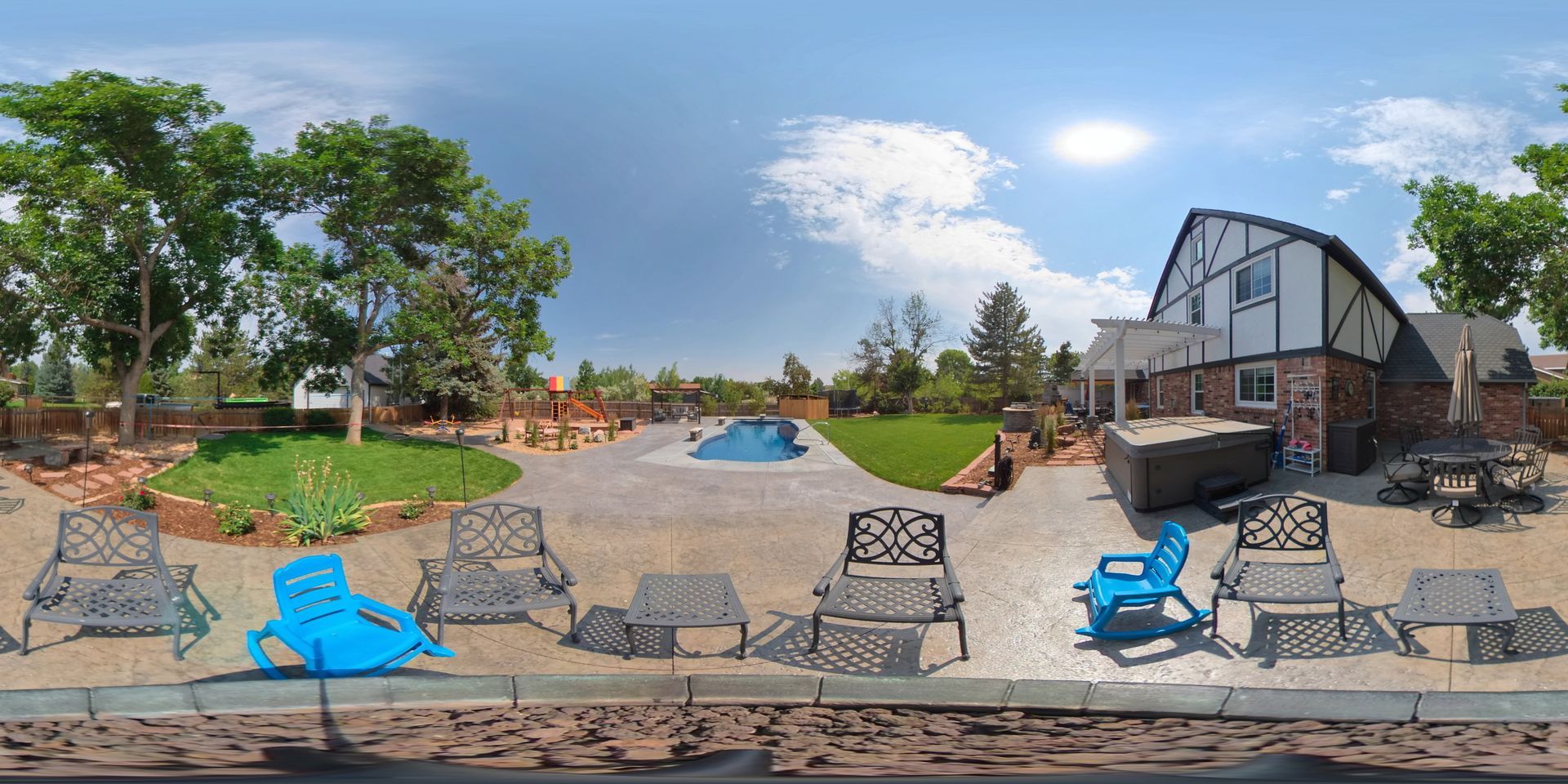 Backyard with pool, trees, and Tudor-style house; blue lounge chairs on gravel patio.