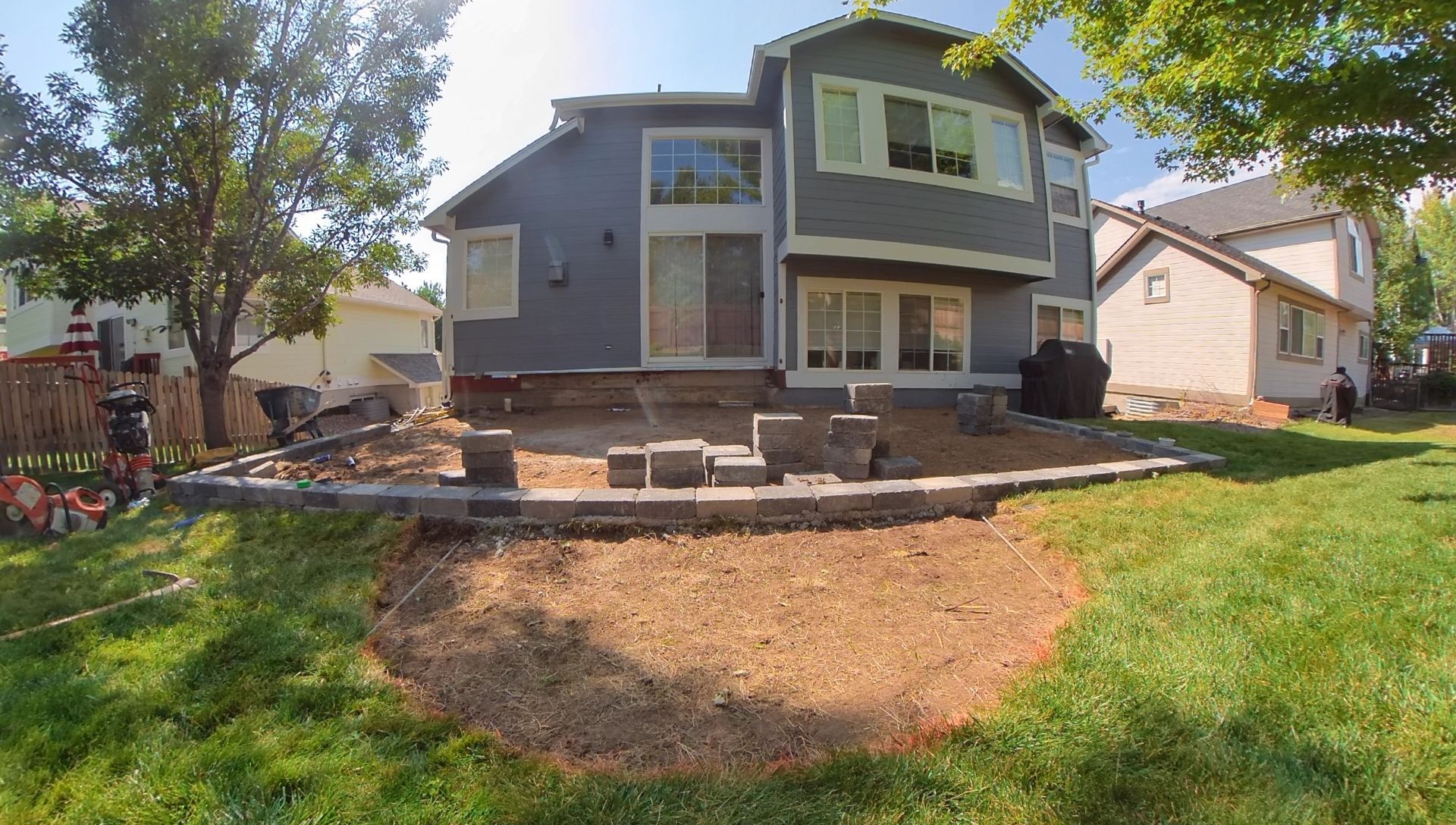 Backyard with house and patio construction; brown dirt, grass, gray siding.