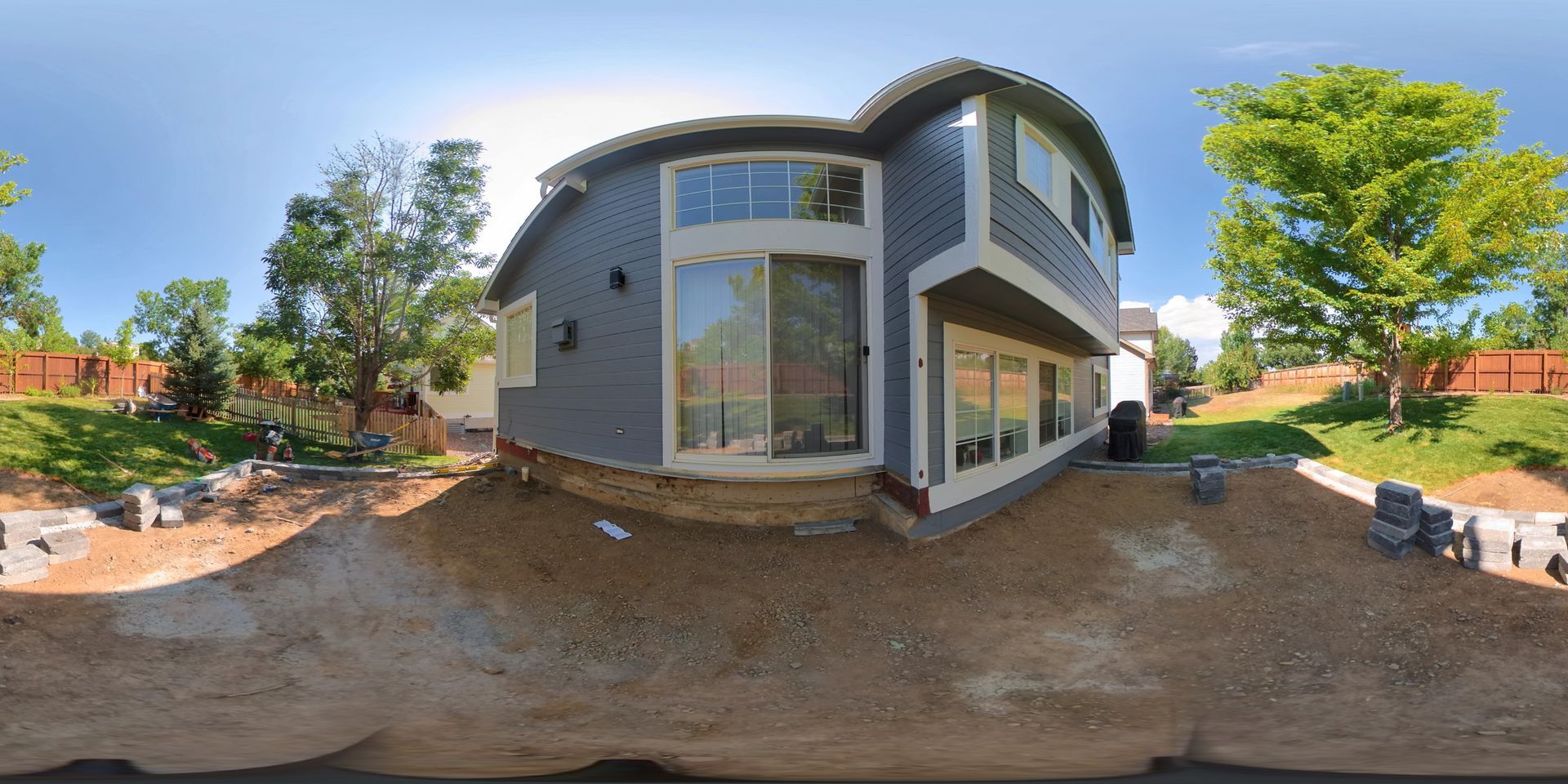 House exterior with a blue sky, trees, and dirt landscaping.
