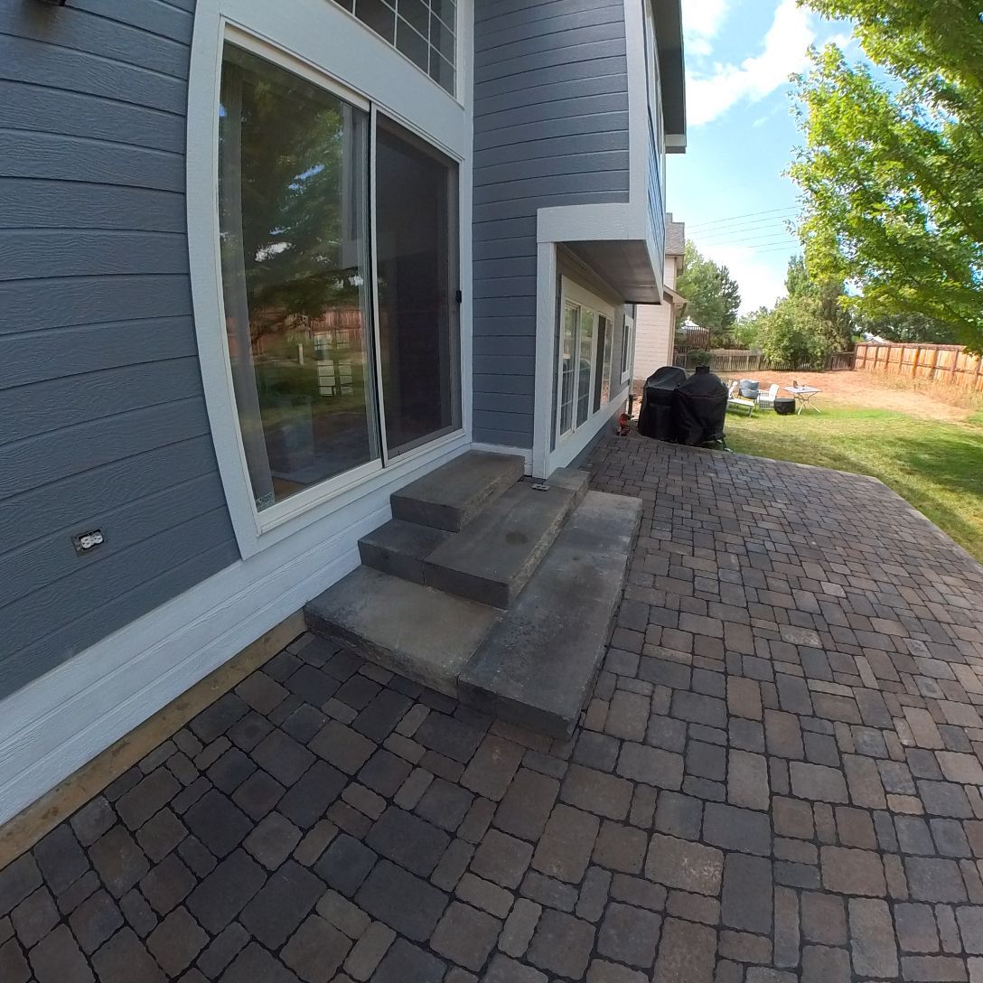 Blue house exterior with patio, steps, and sliding glass door. A barbecue grill and trees are in the yard.