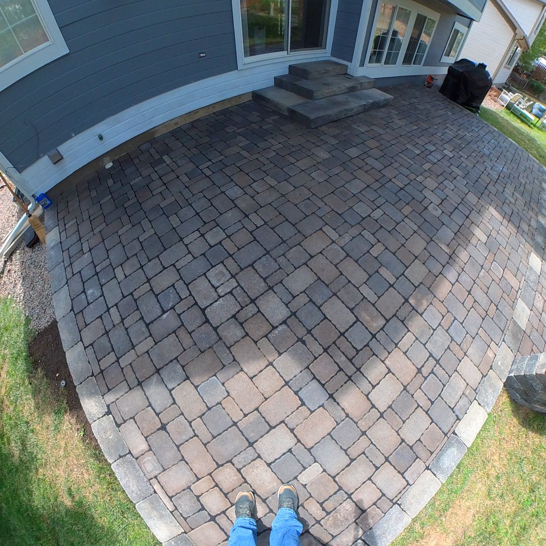 Person standing on a paver patio outside a house. Blue jeans and feet visible.