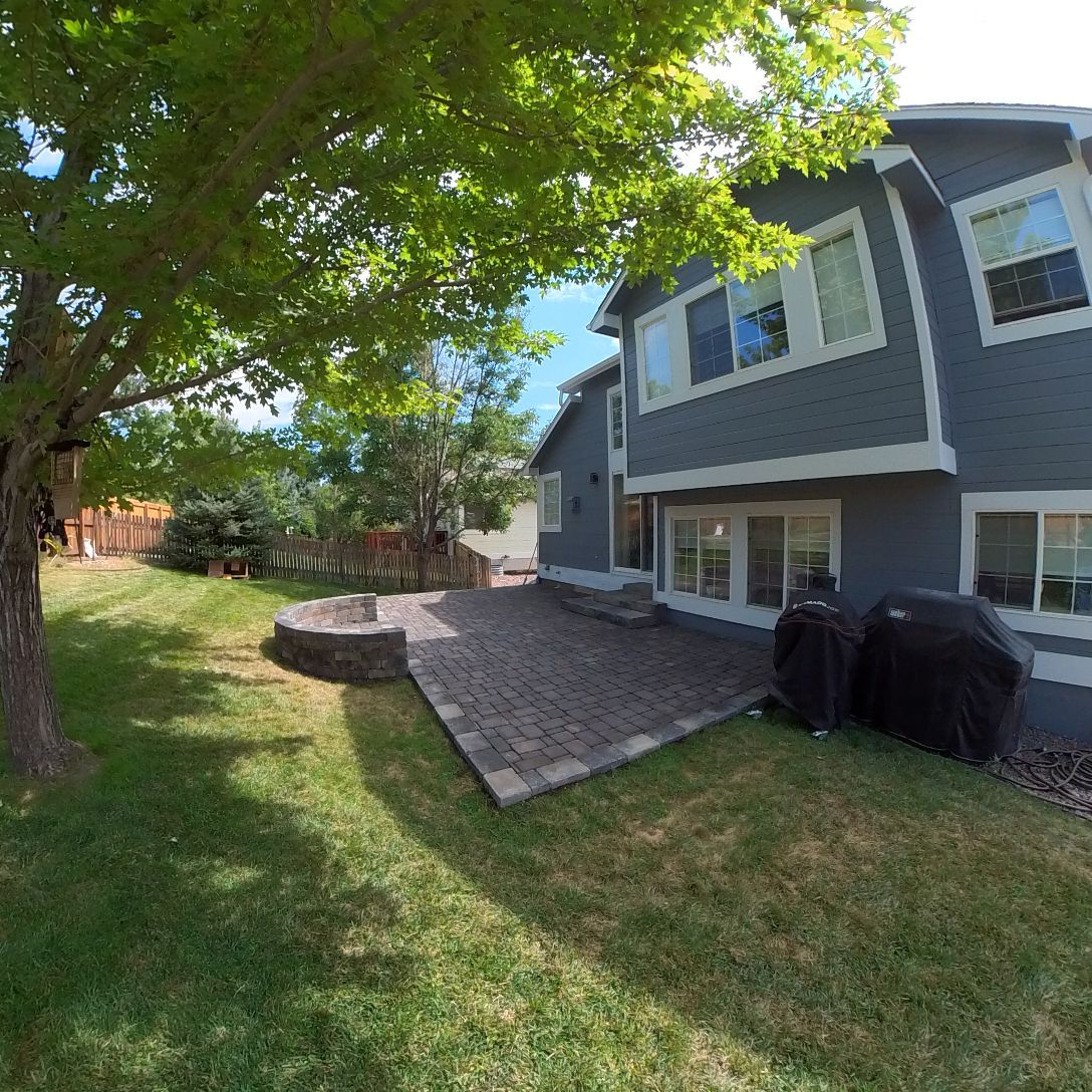Backyard with patio, fire pit, and a gray house with windows under a bright blue sky.