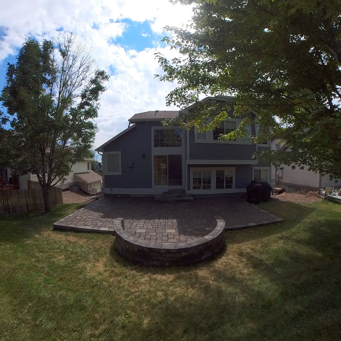 Blue house with a stone patio and fire pit in a grassy backyard, under a blue sky.