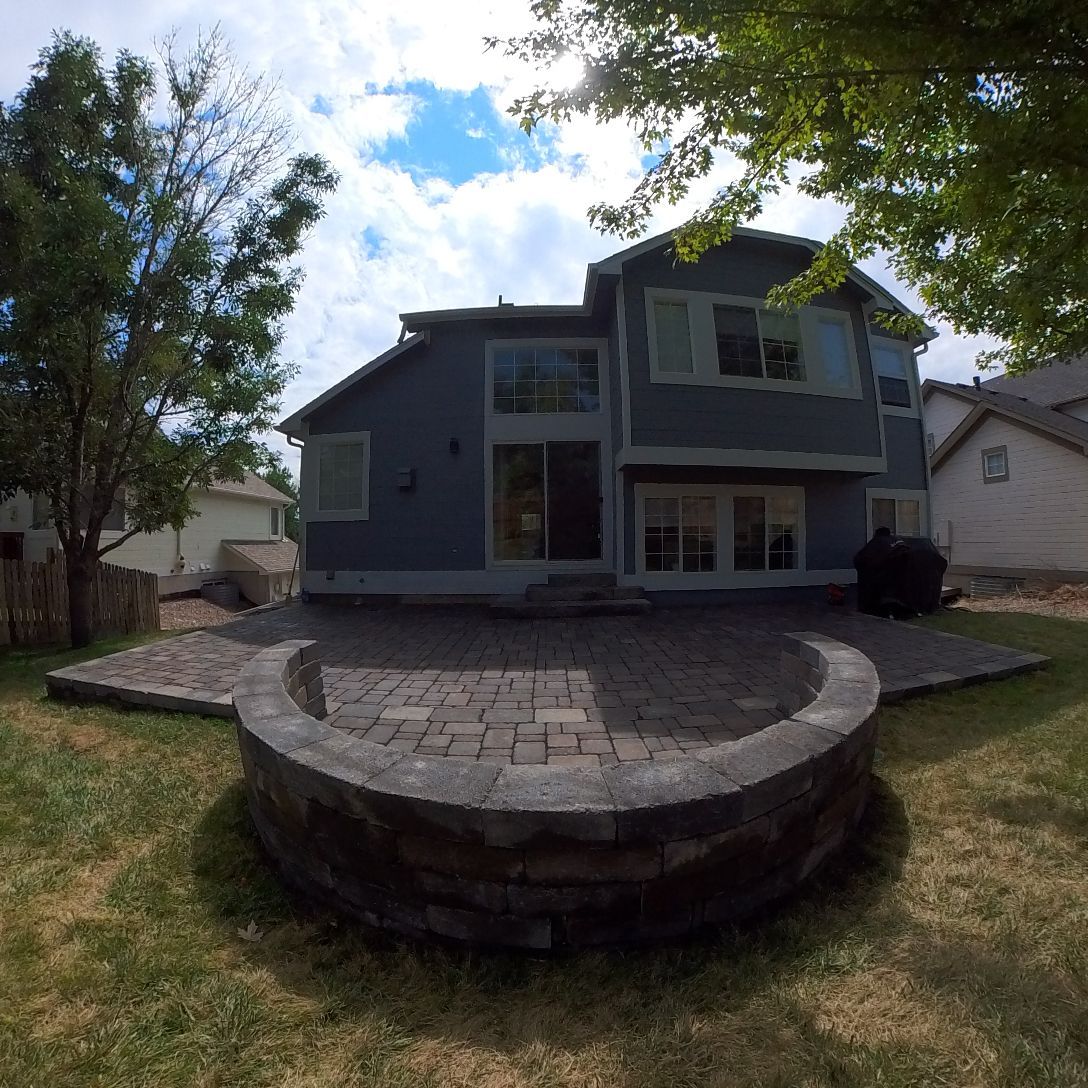 Backyard with a gray house, patio, fire pit, and blue sky.
