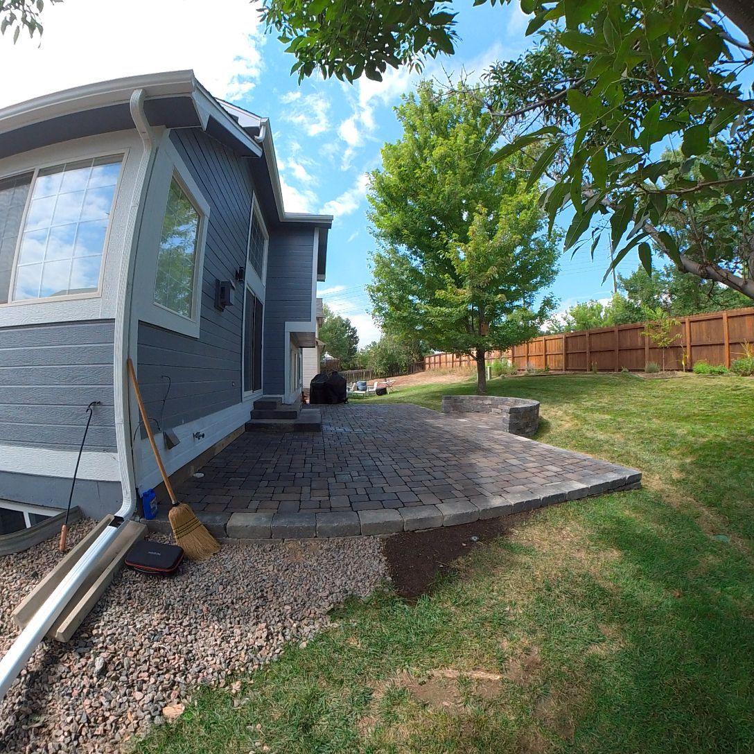 Backyard patio with a blue house, grass, and a wooden fence on a sunny day.