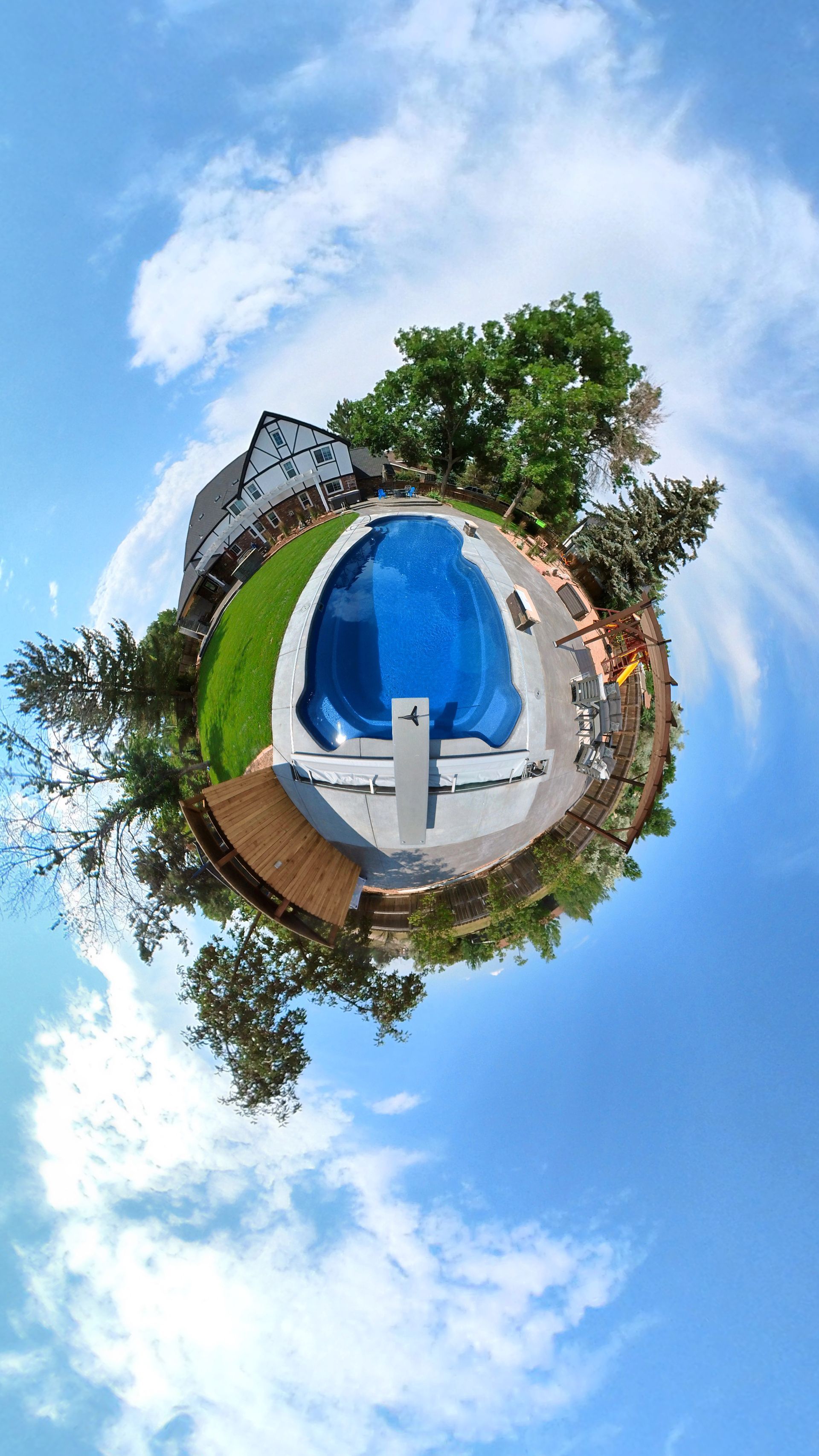 Tiny planet view of a pool, house, and trees under a blue sky with clouds.