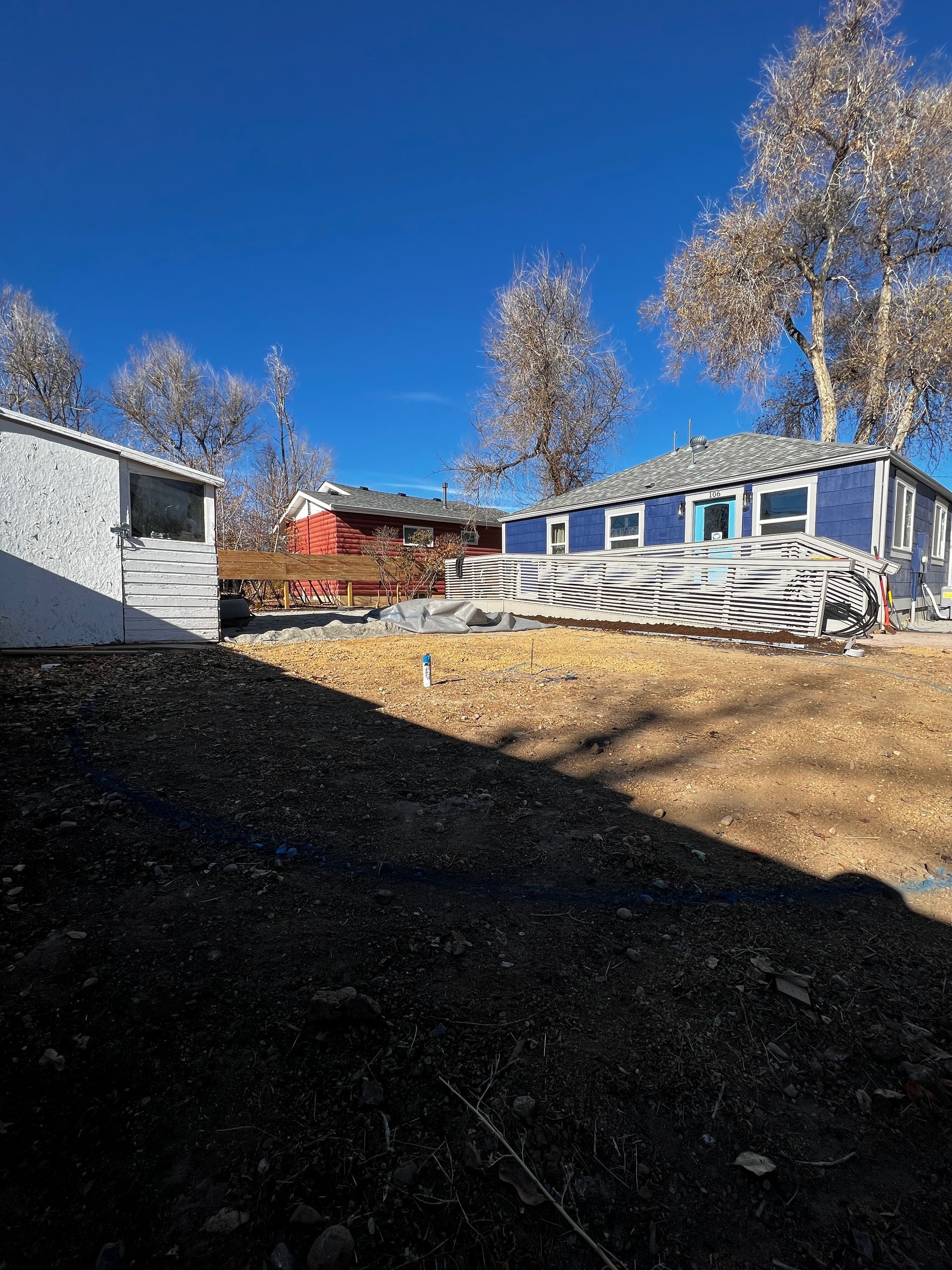 A blue house with bare trees under a clear, blue sky.