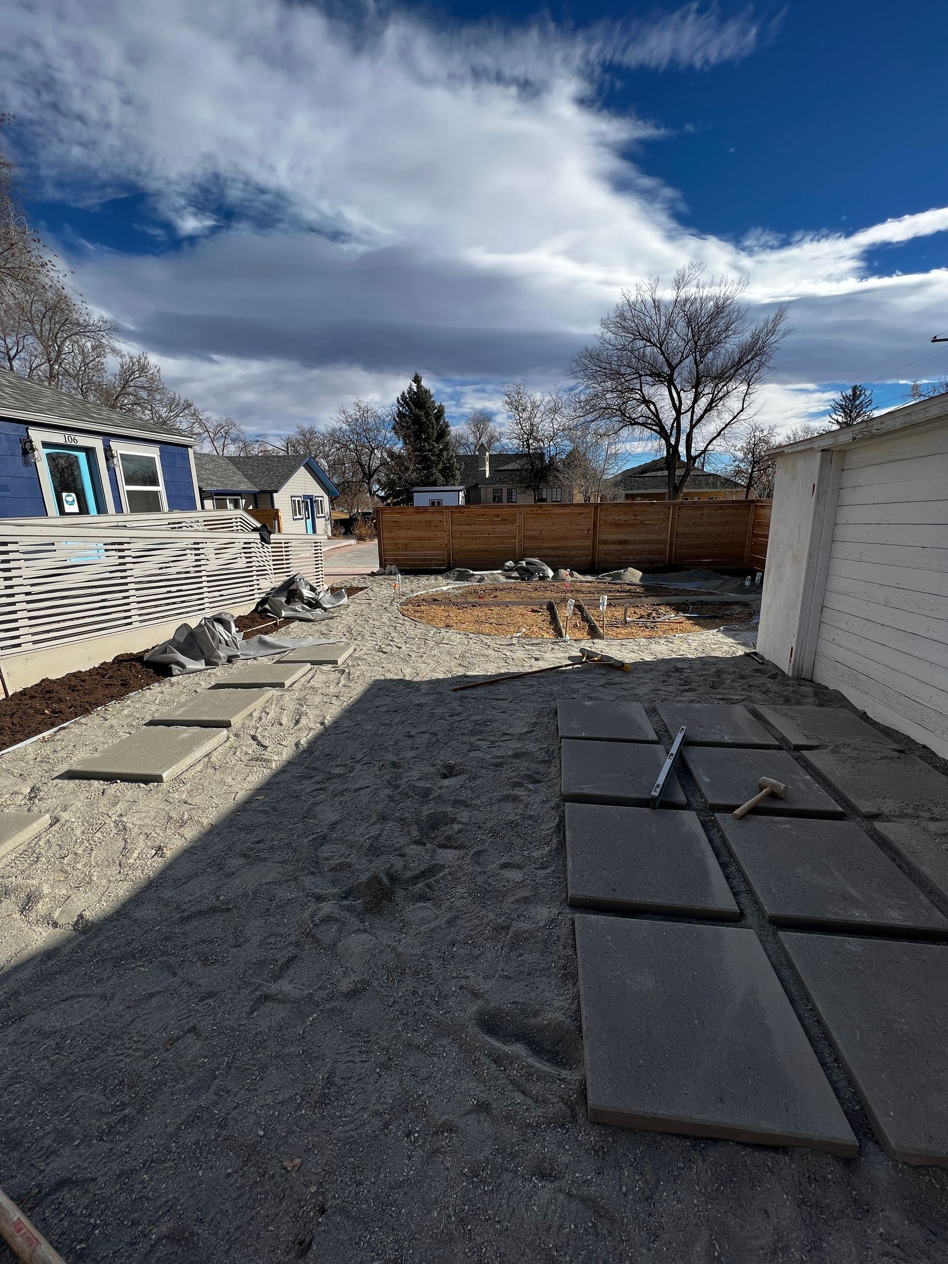 Backyard under construction with stepping stones, gravel, wooden fence, and blue house.