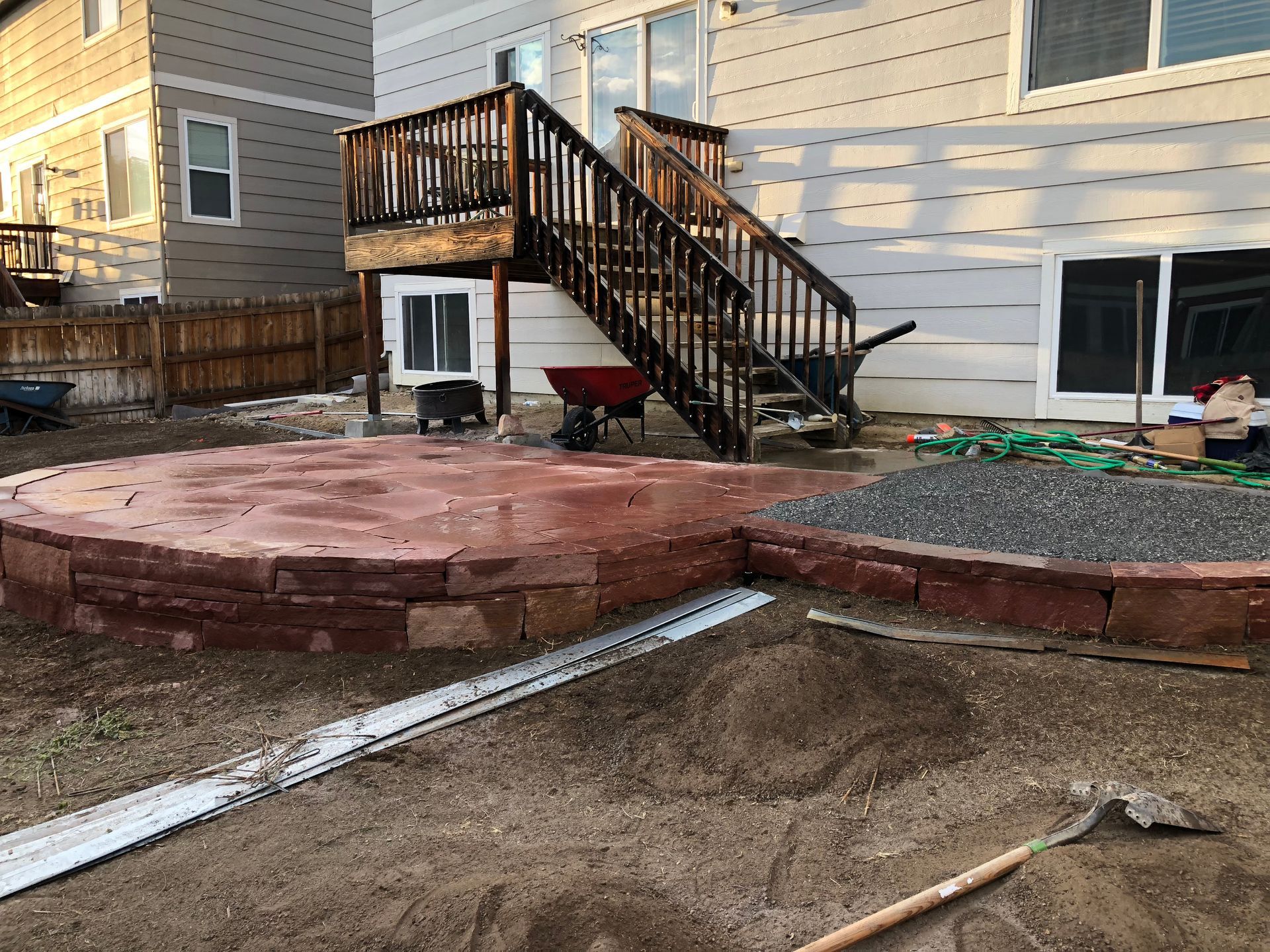 Backyard patio construction with brick borders, red paving stones, wooden deck and stairs.