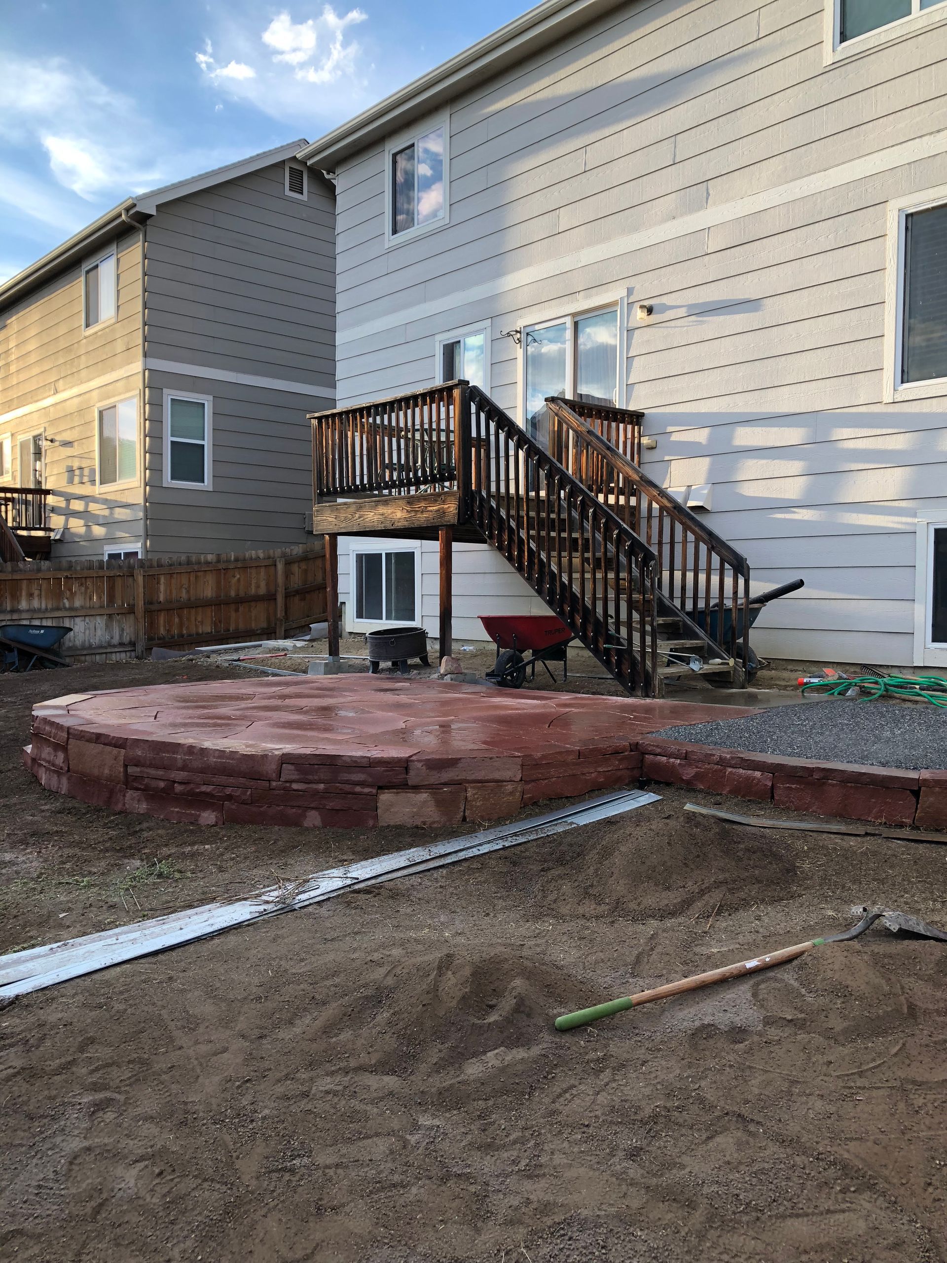 A backyard with a raised patio, wooden deck, and a two-story house.