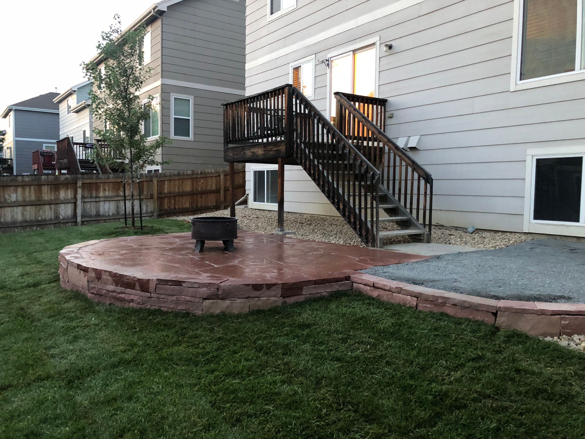 Backyard patio with fire pit, wooden stairs leading to a deck, and a grass lawn.