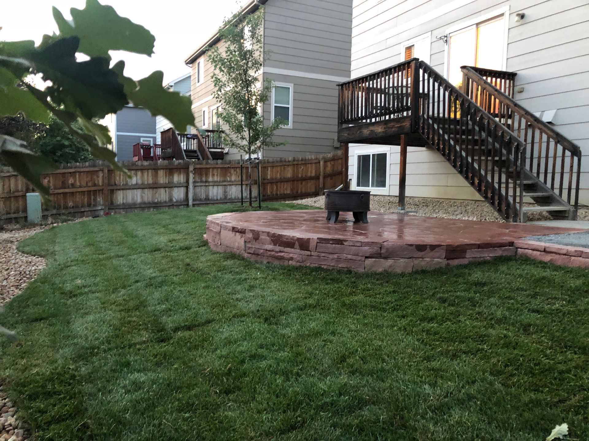 Lush green backyard with a brick fire pit and wooden deck.
