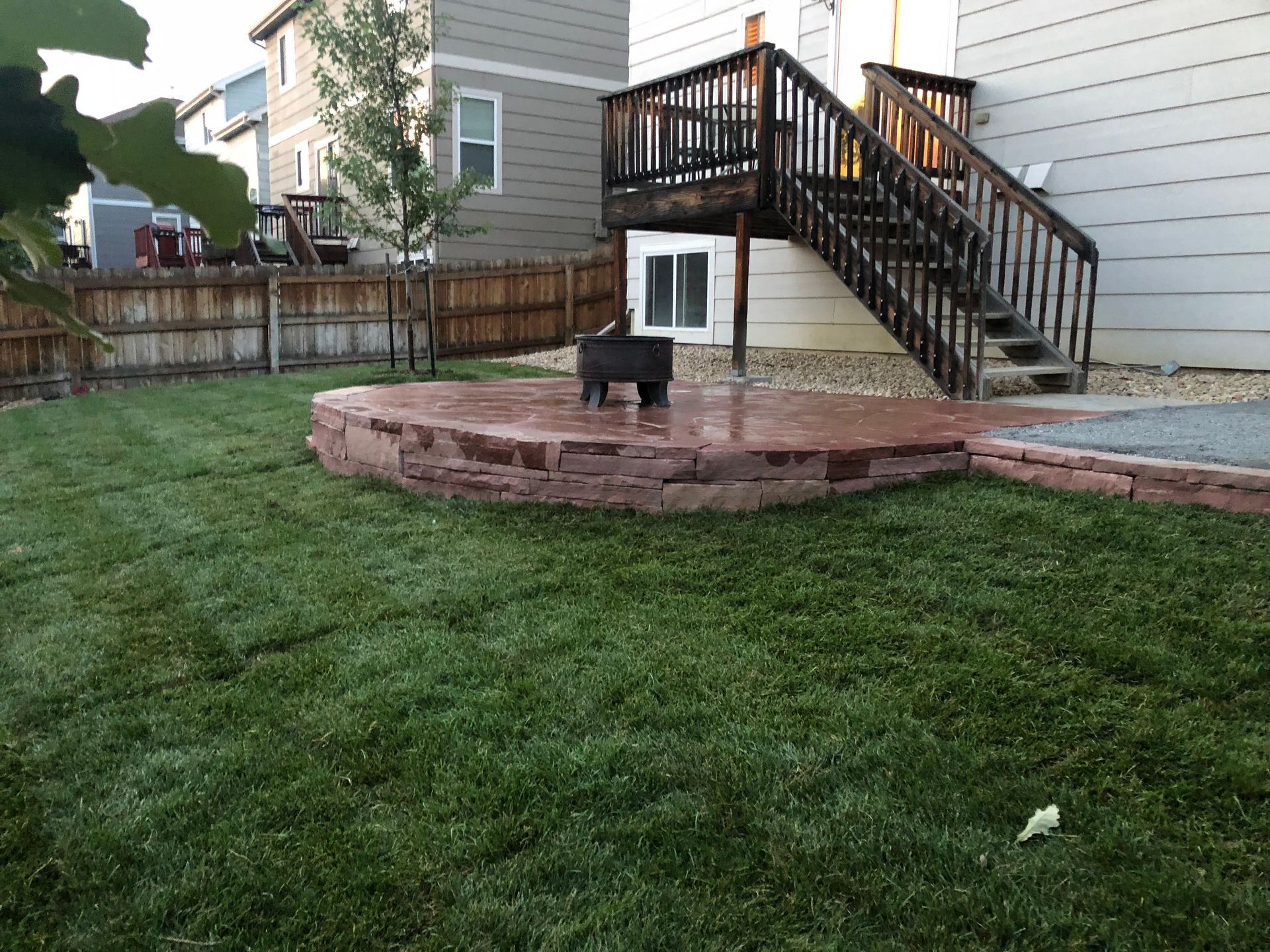 Backyard with a brick patio, fire pit, stairs to a deck, and green lawn.