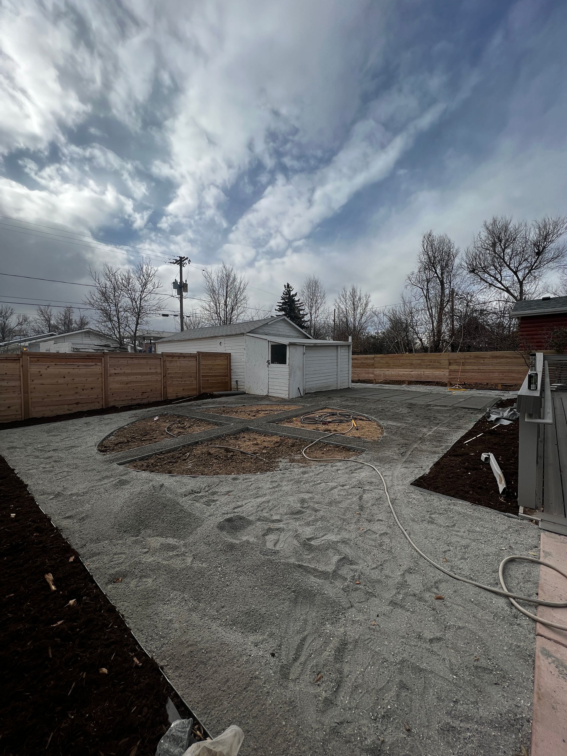 Backyard with gravel, shed, wooden fence, cloudy sky.