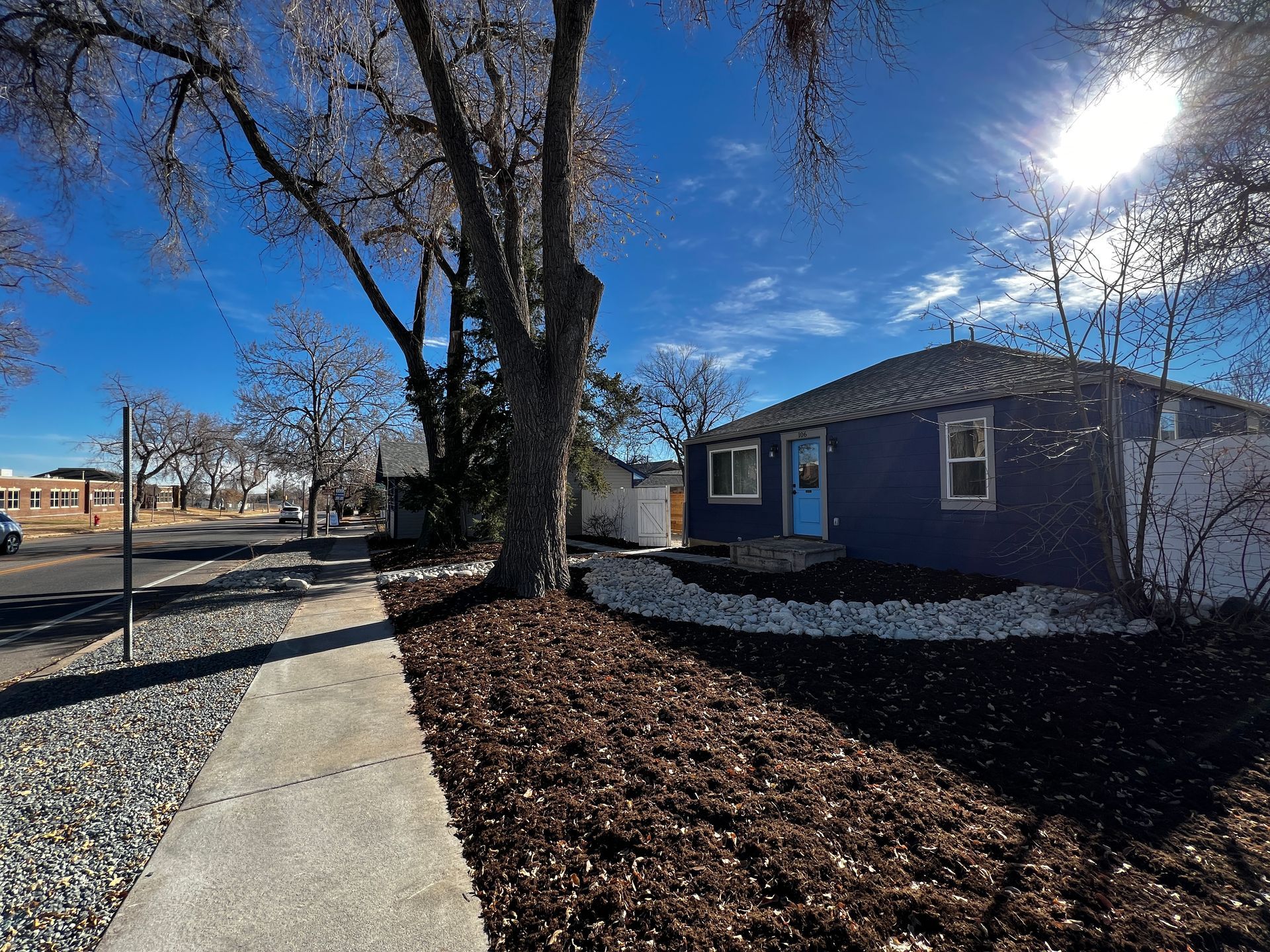 Blue house with a bright blue door on a sunny day with trees and a sidewalk.