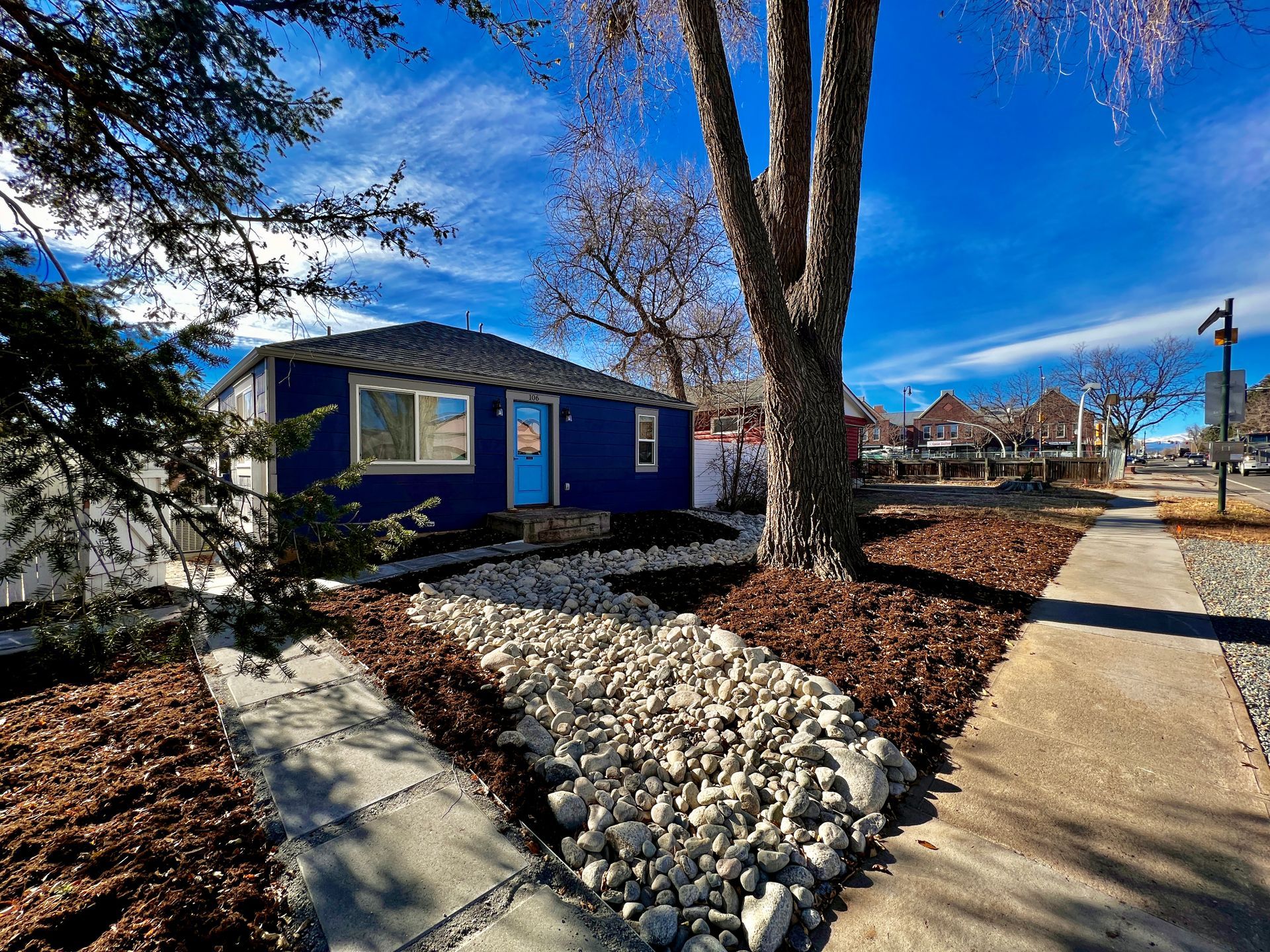Blue house with white rocks, sidewalk, and street under a blue sky.