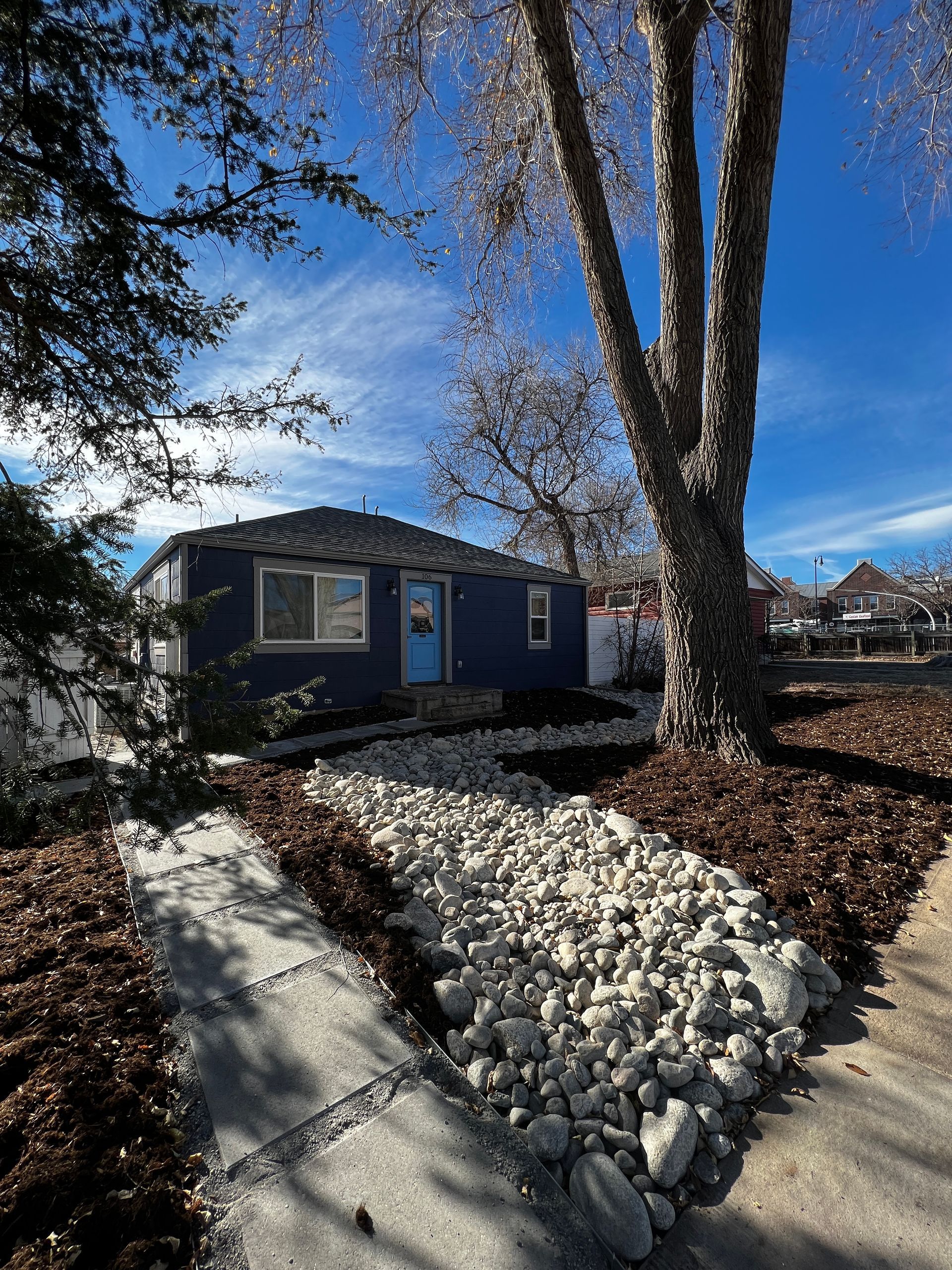 Blue house with landscaped yard and large tree on a sunny day.