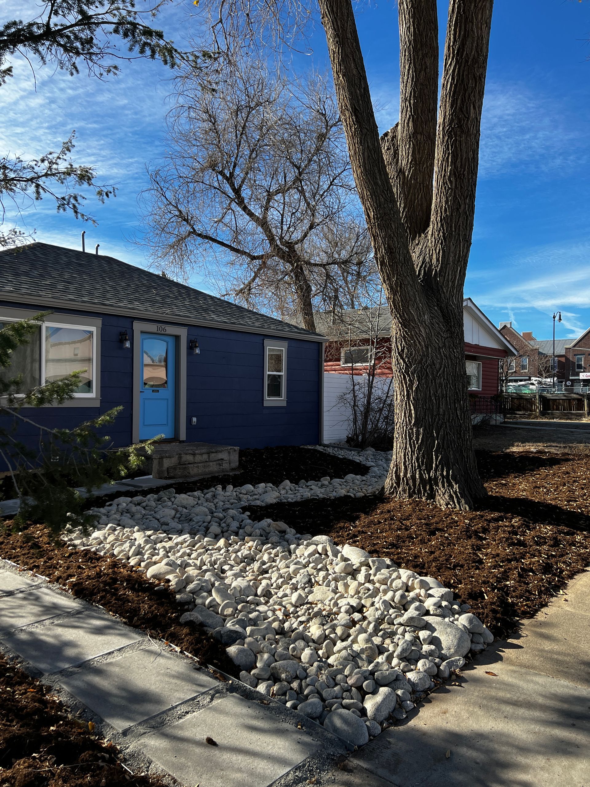 Blue house with light blue door, gray stone path, and tree on a sunny day.
