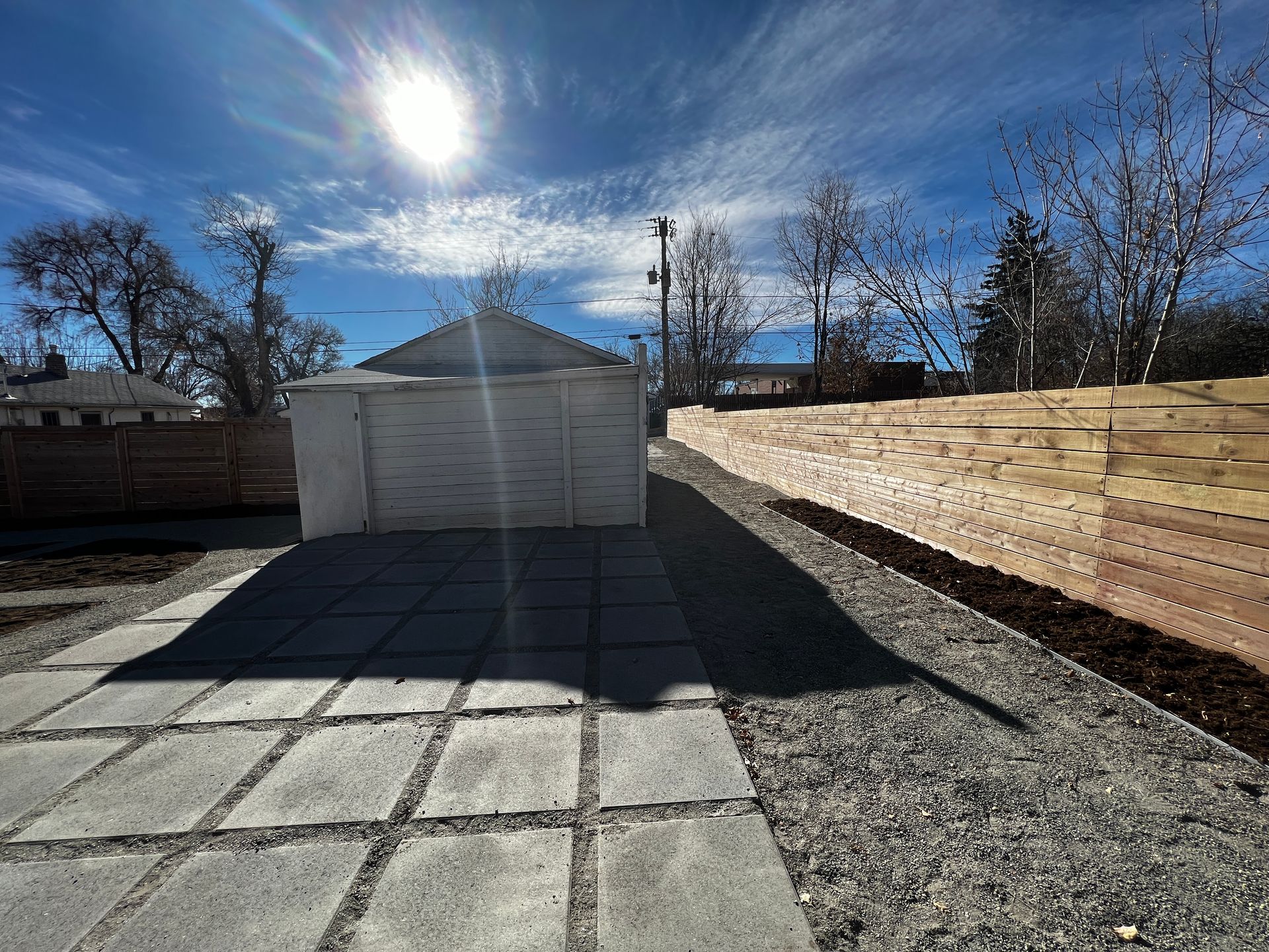 Backyard with stone patio, gravel, and a small white garage on a sunny day.