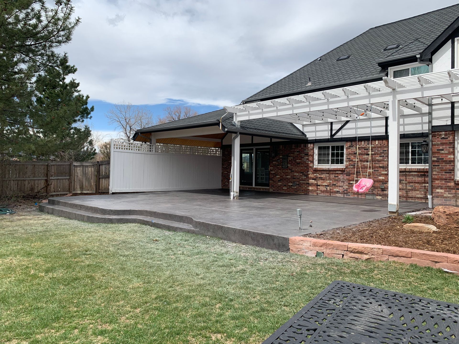 Backyard patio with a brick house, a pergola, and a swing set.